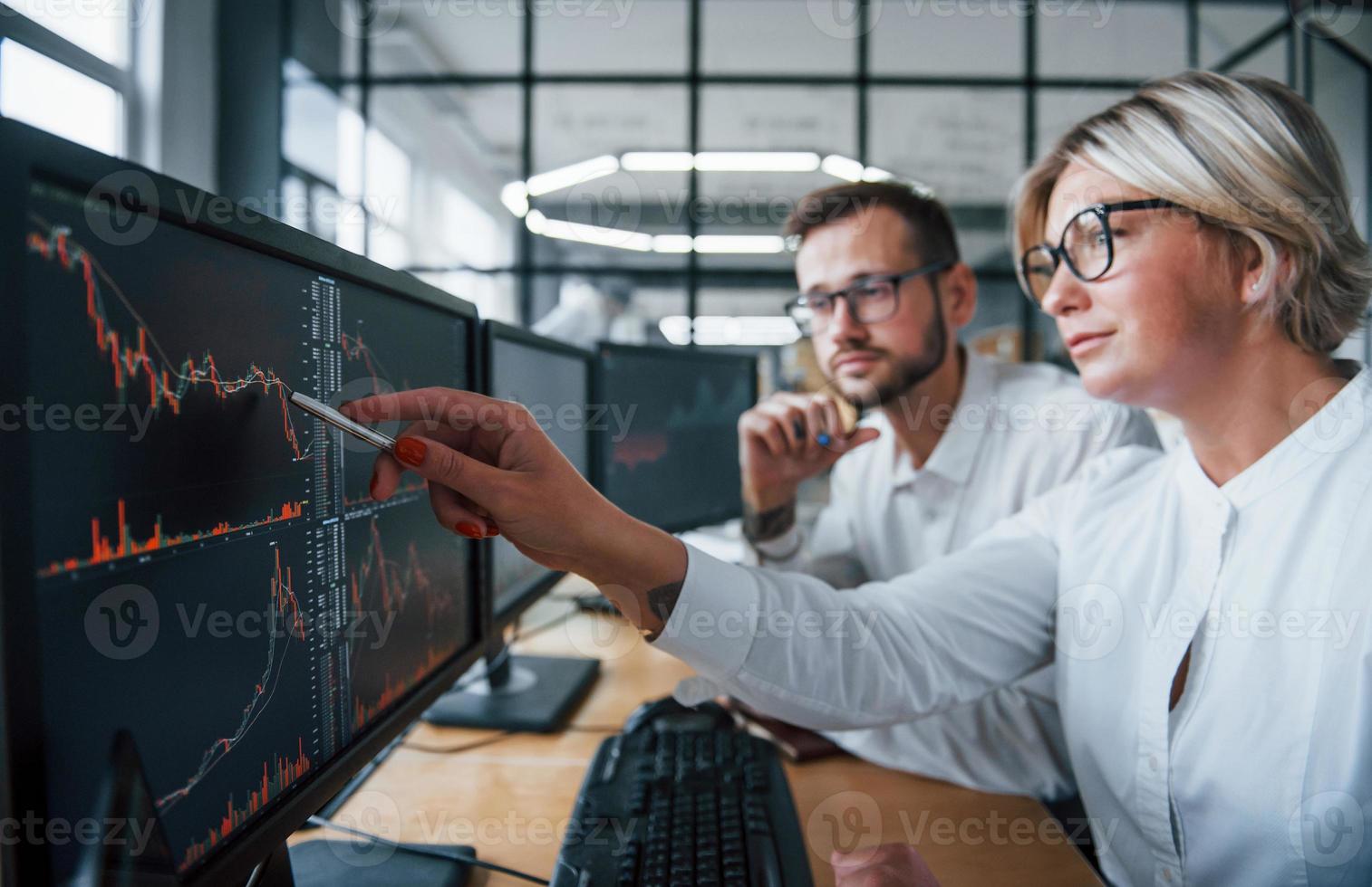 Puts pen to the display. Two stockbrokers in formal clothes works in the office with financial market photo