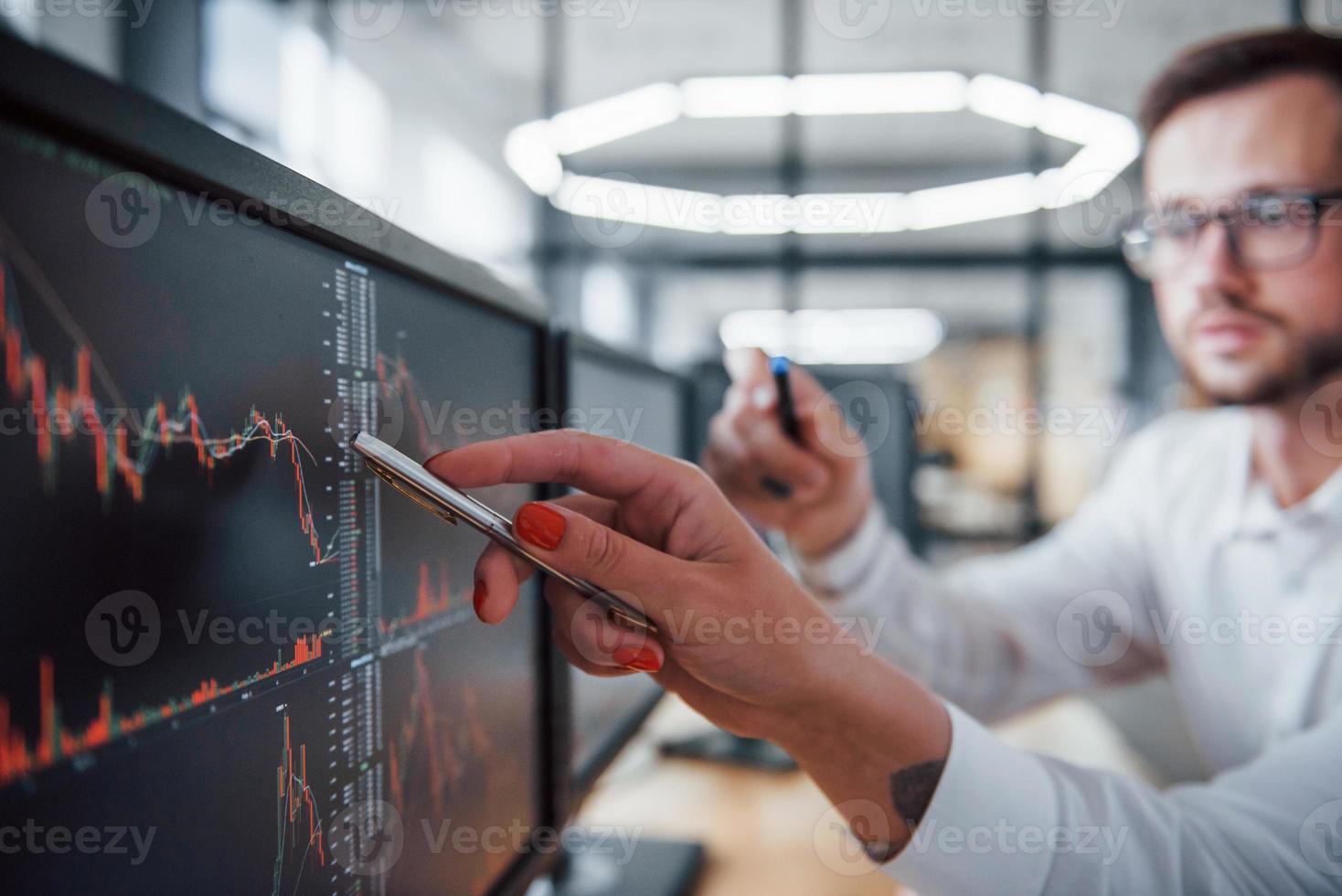 Puts pen to the display. Two stockbrokers in formal clothes works in the office with financial market photo