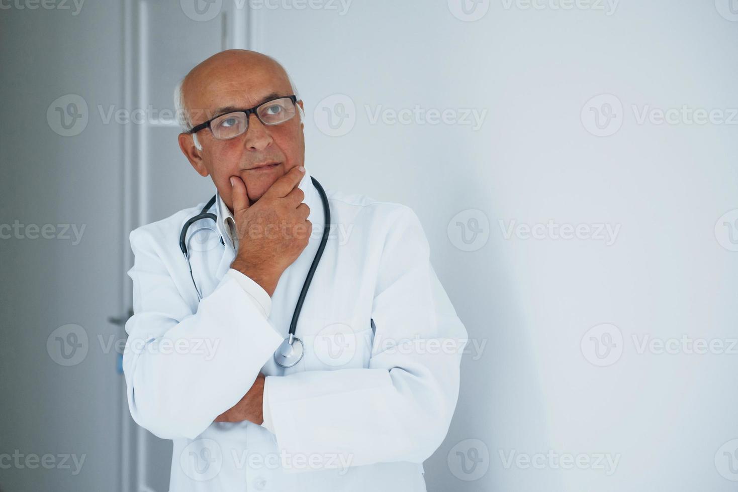 Portrait of senior doctor in white uniform that stands in the clinic photo