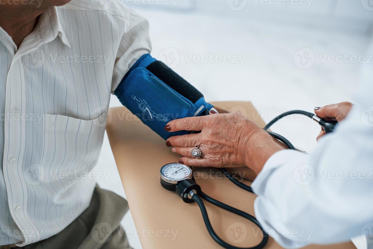 Close up view. Female doctor uses tonometer to make blood pressure measuring to senior man photo