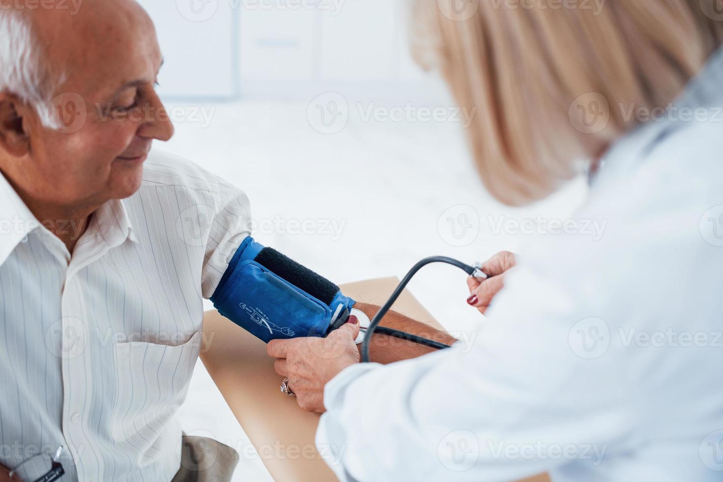 Female doctor uses tonometer to make blood pressure measuring to senior man photo
