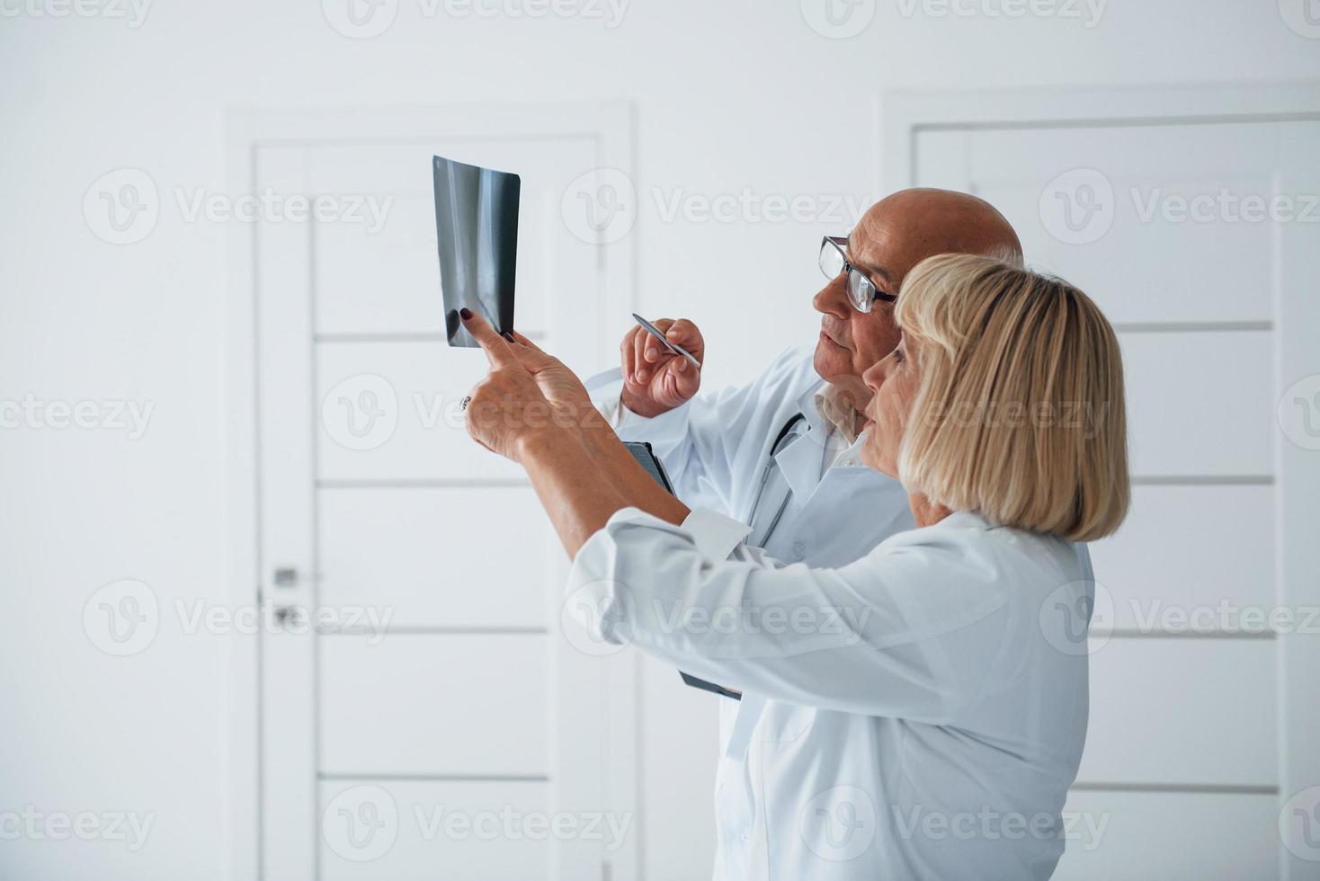 Senior man and woman doctors in white uniform examines x-ray of human legs photo