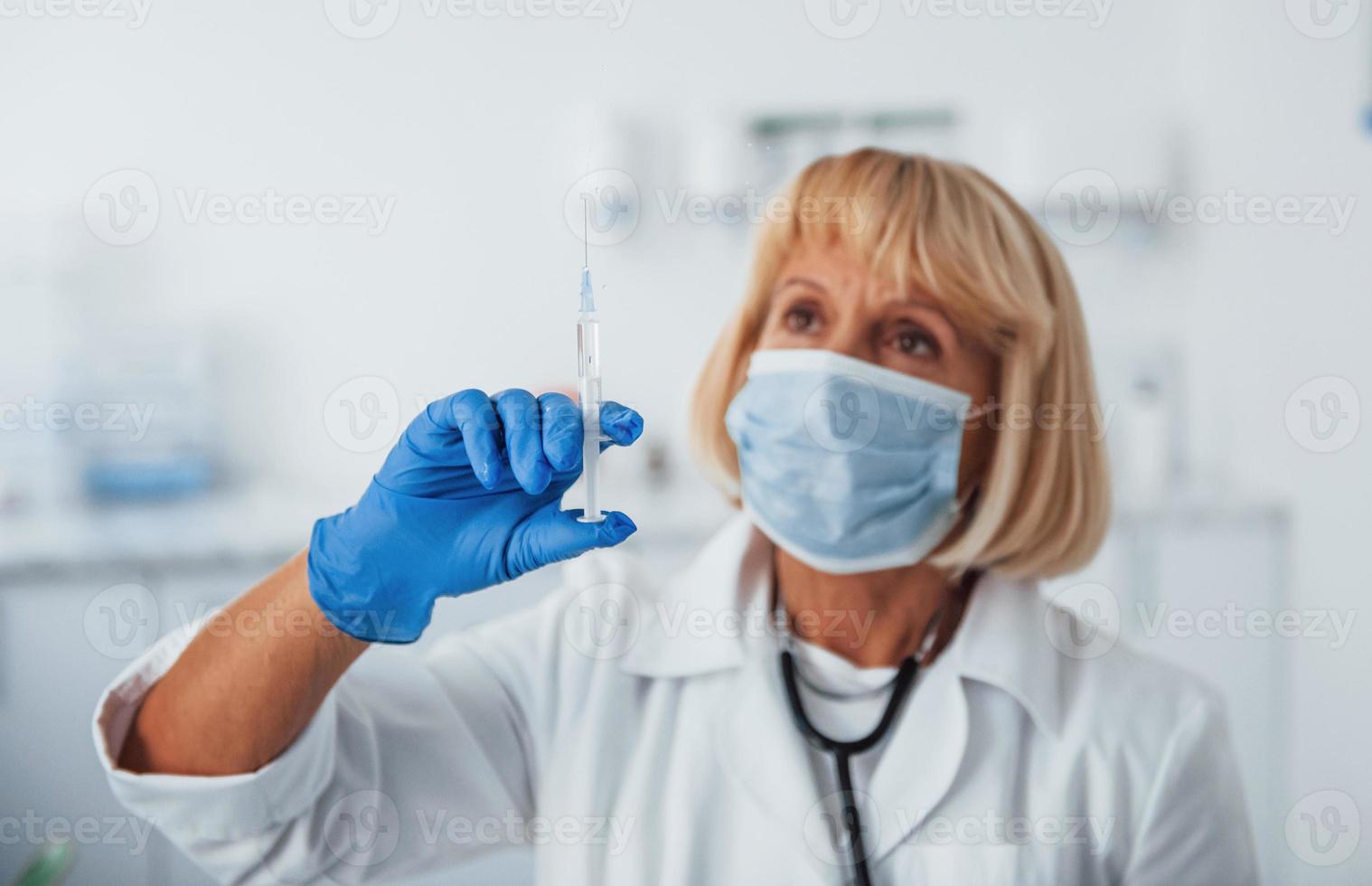 Portrait of senior female doctor in mask with syringe full of liquid photo