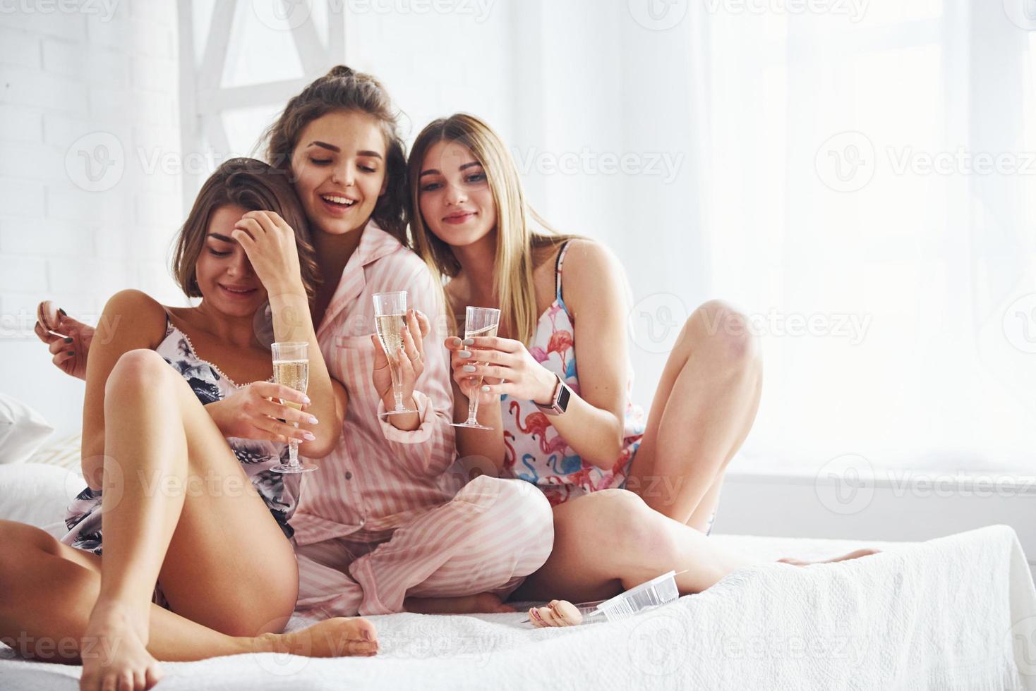celebrando con vasos de alcohol en las manos. amigas felices pasando un buen rato en la fiesta de pijamas en el dormitorio foto