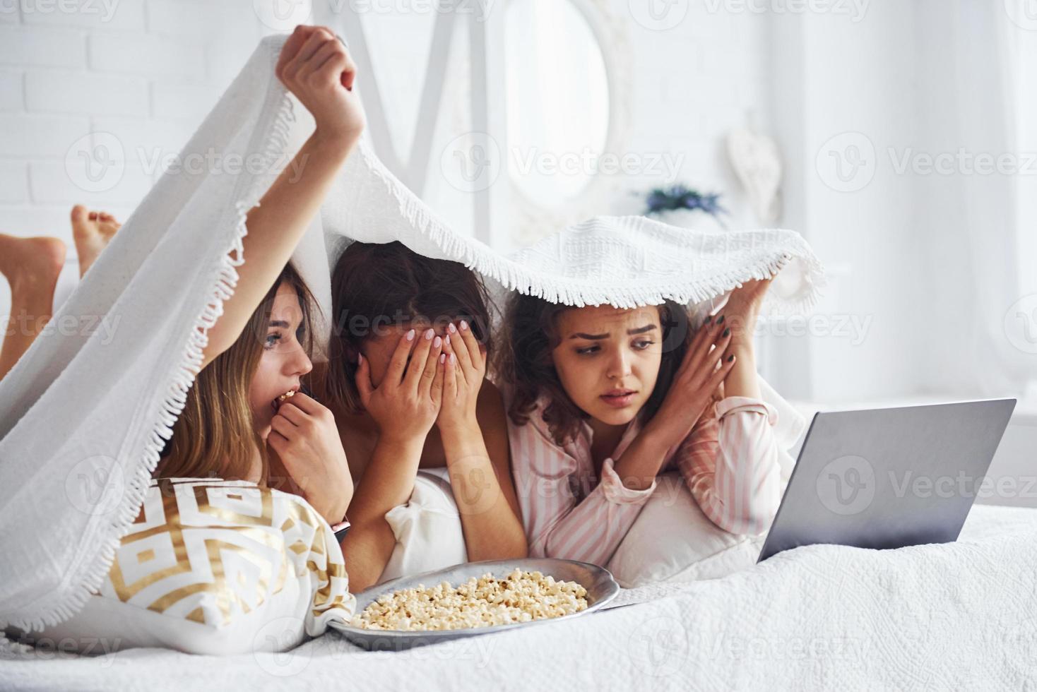 Watching scary movie. Happy female friends having good time at pajama party in the bedroom photo