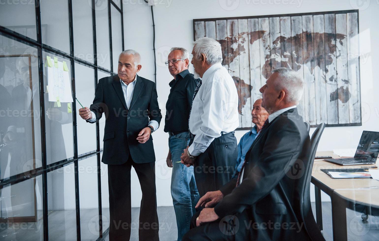 trabajando con pegatinas sobre vidrio. un equipo anciano de arquitectos de hombres de negocios mayores tiene una reunión en la oficina foto