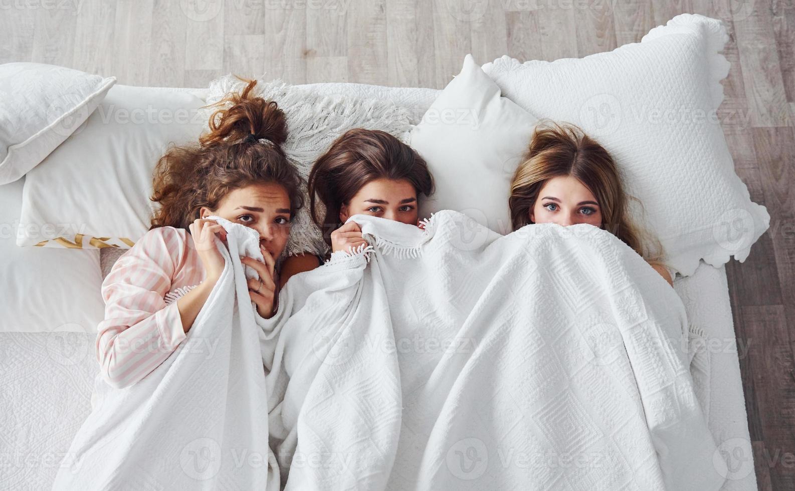 escondido debajo de la manta. amigas felices pasando un buen rato en la fiesta de pijamas en el dormitorio foto