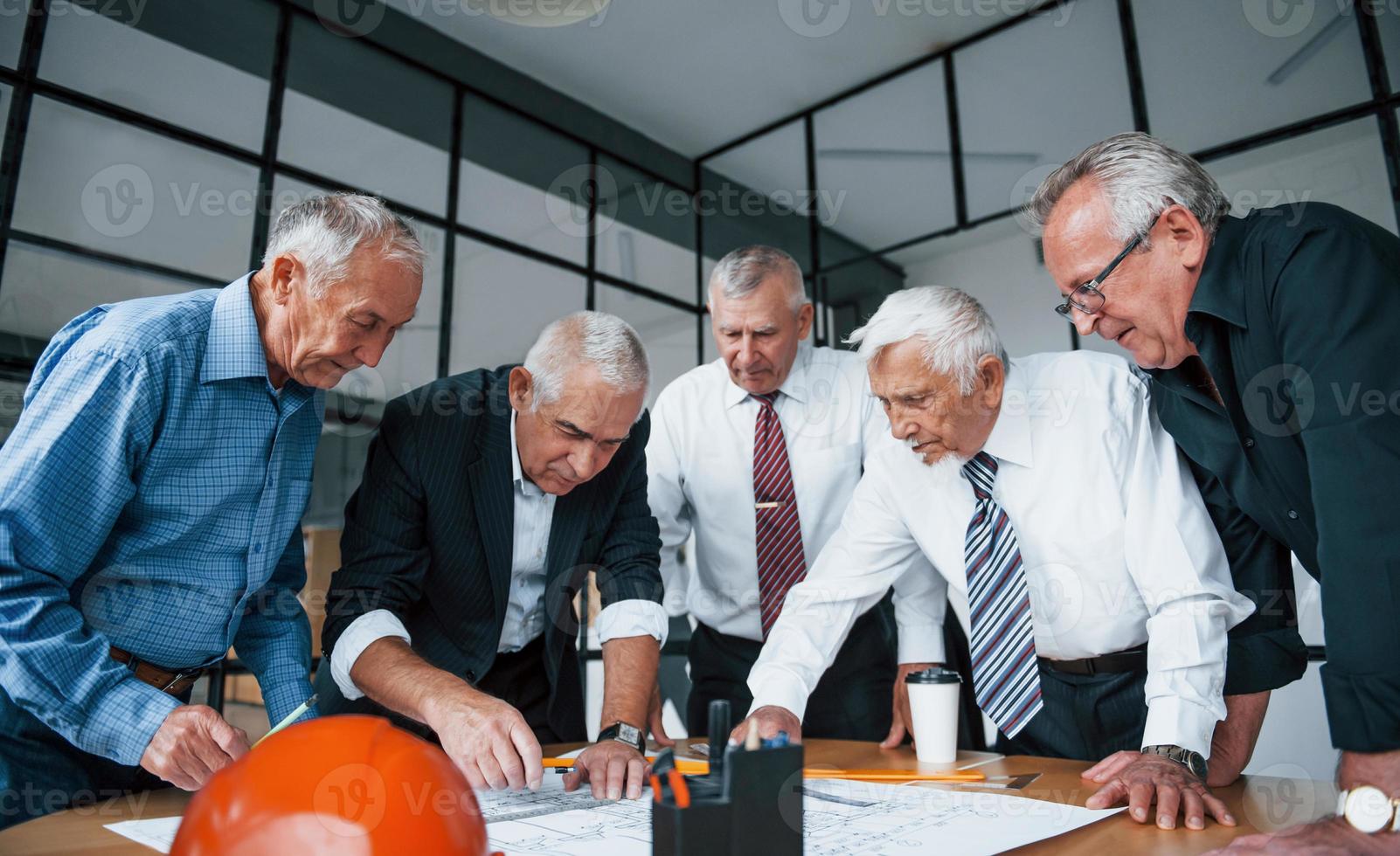 Aged team of elderly businessman architects works with plan in the office photo