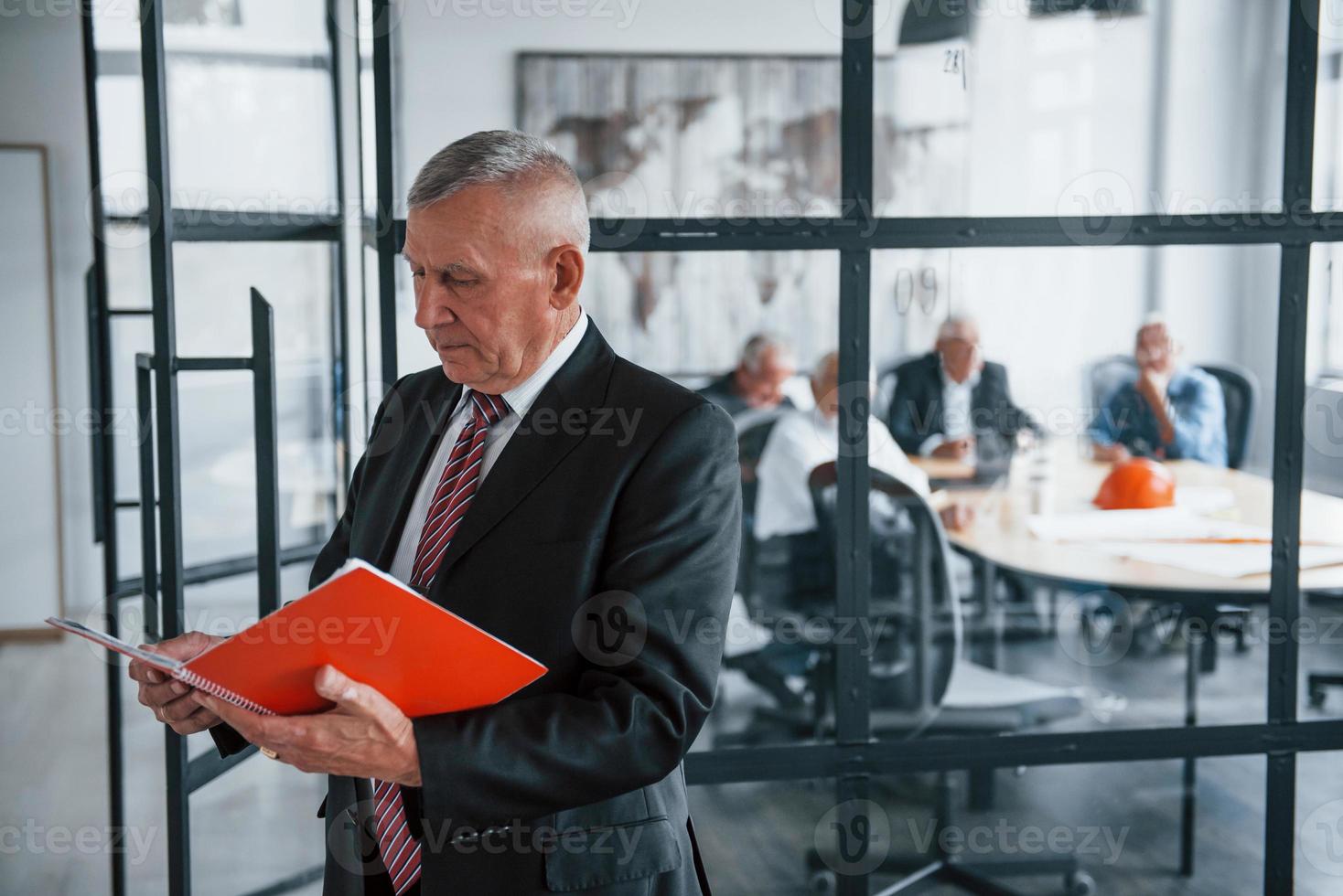 Portrait of senior man that stands in front of aged team of elderly businessman architects that have a meeting in the office photo