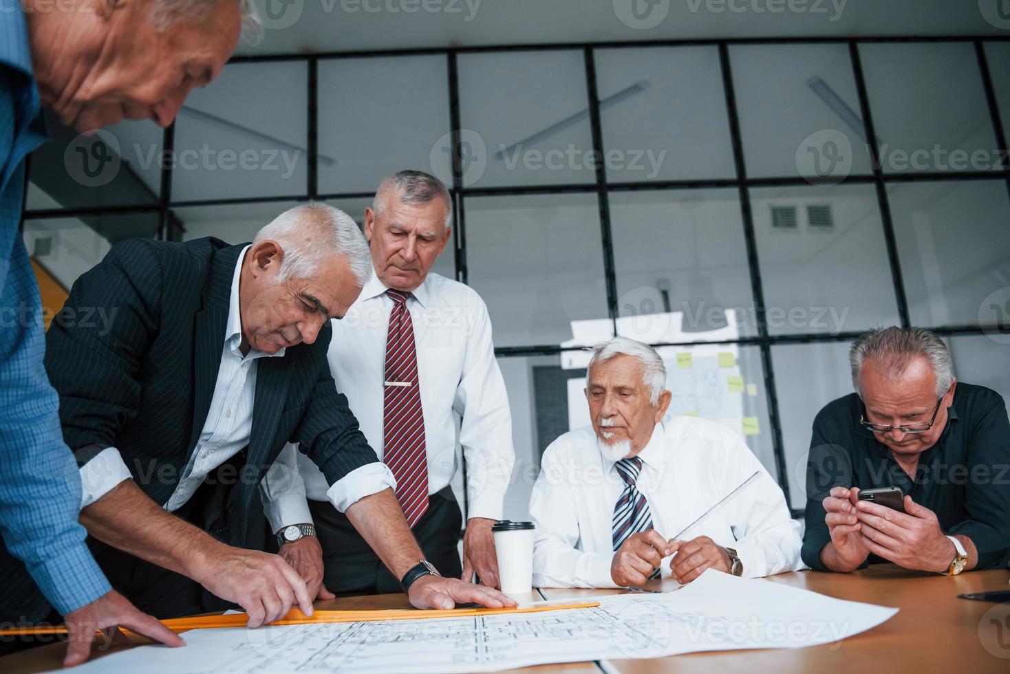planificar la construcción midiéndola en papel. un equipo de ancianos arquitectos de hombres de negocios tiene una reunión en la oficina foto