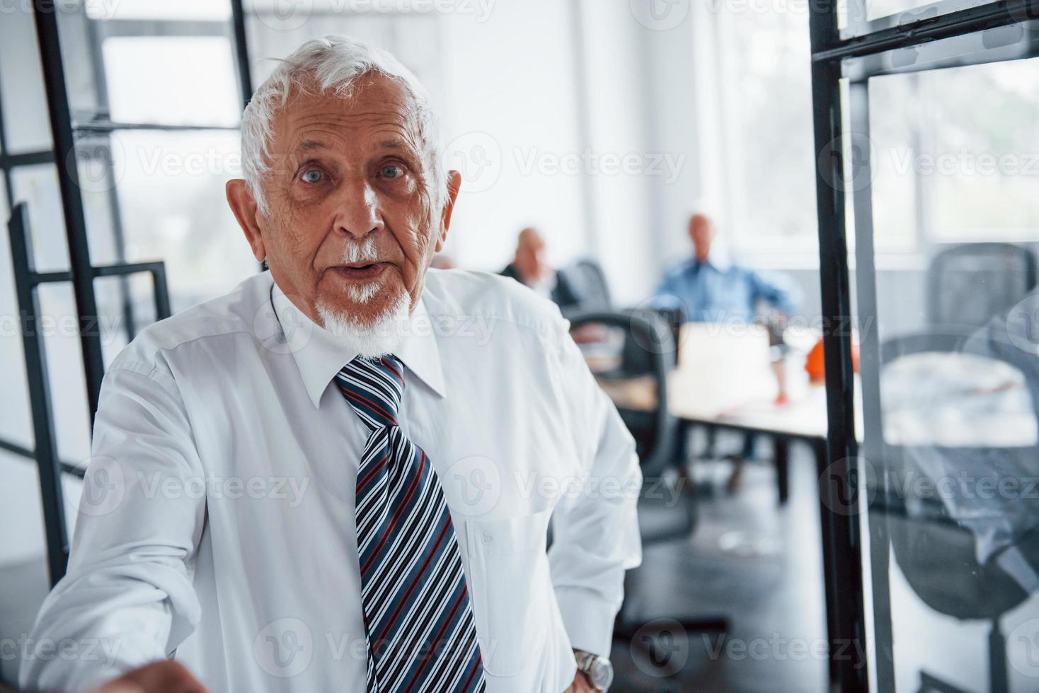 Portrait of senior man that stands in front of aged team of elderly businessman architects that have a meeting in the office photo