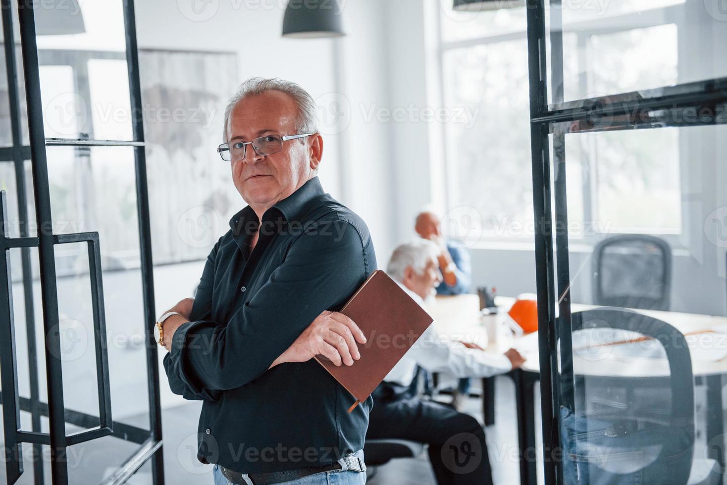 Portrait of senior man that stands in front of aged team of elderly businessman architects that have a meeting in the office photo