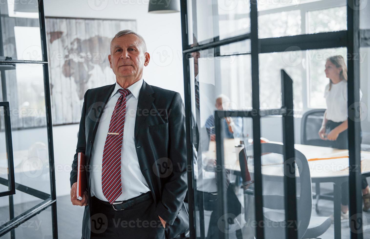 Portrait of senior man that stands in front of aged team of elderly businessman architects that have a meeting in the office photo