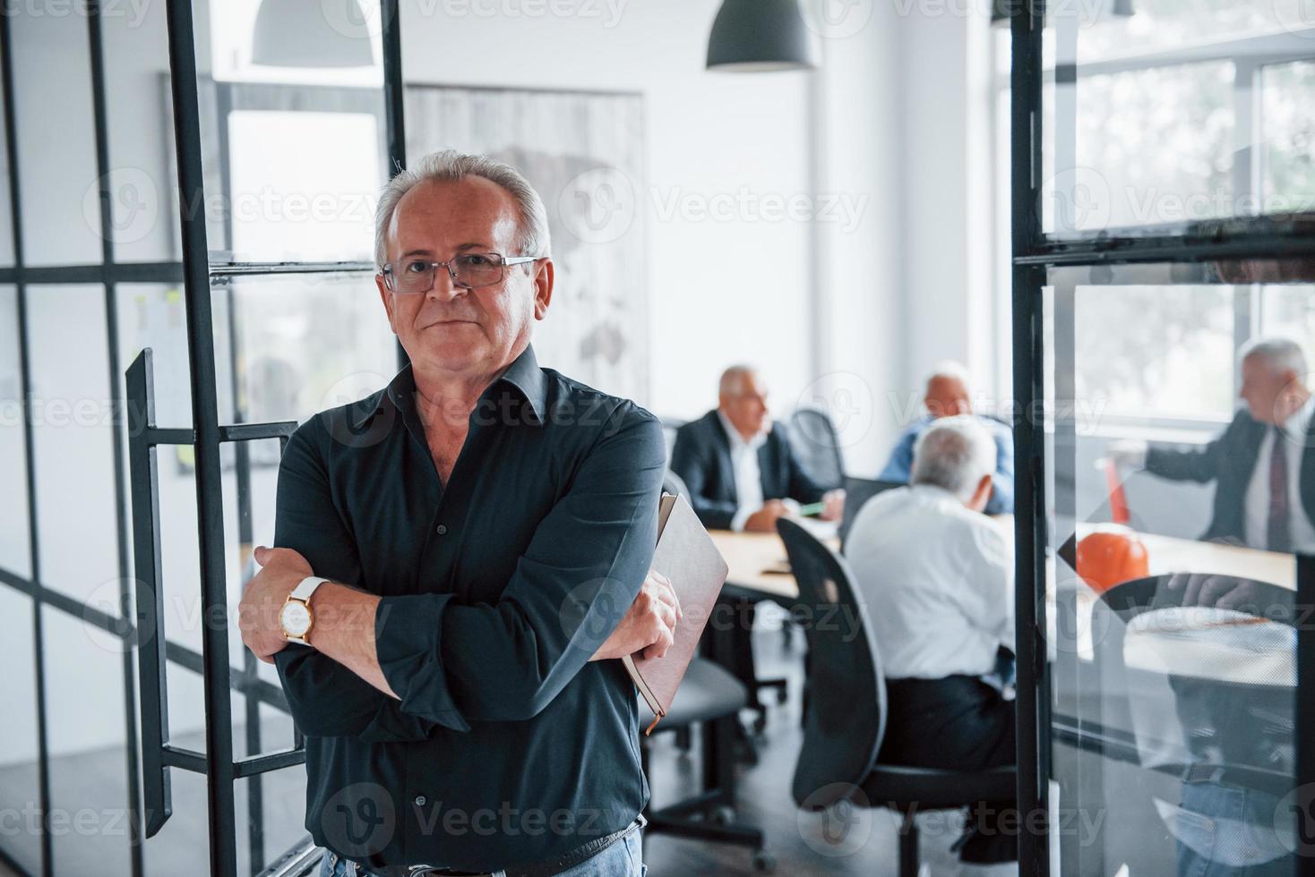 Portrait of senior man that stands in front of aged team of elderly businessman architects that have a meeting in the office photo