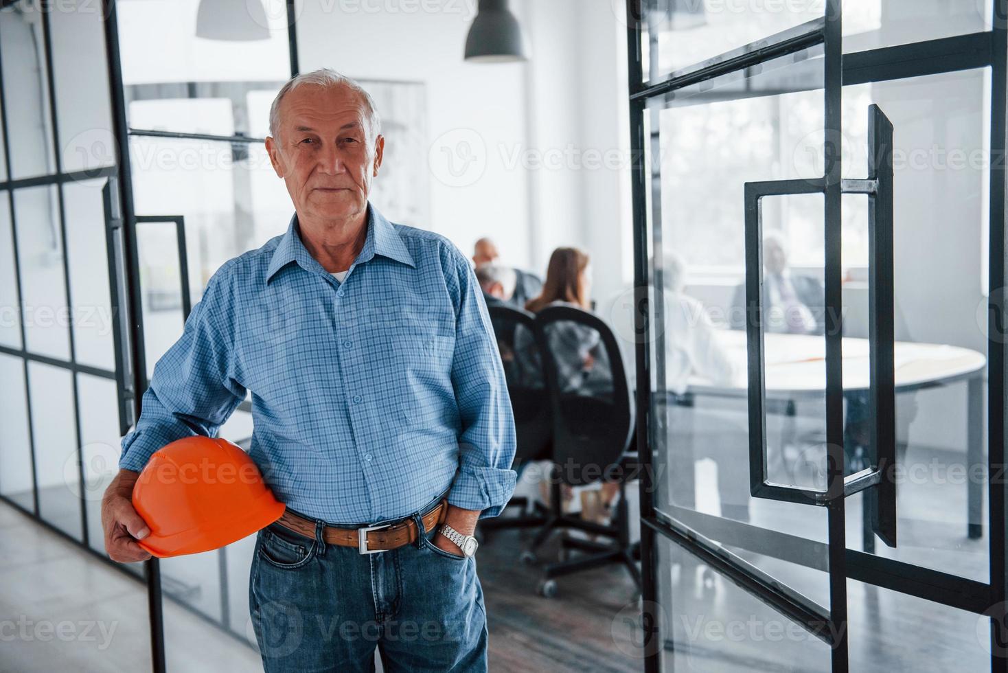 Portrait of senior man that stands in front of aged team of elderly businessman architects that have a meeting in the office photo