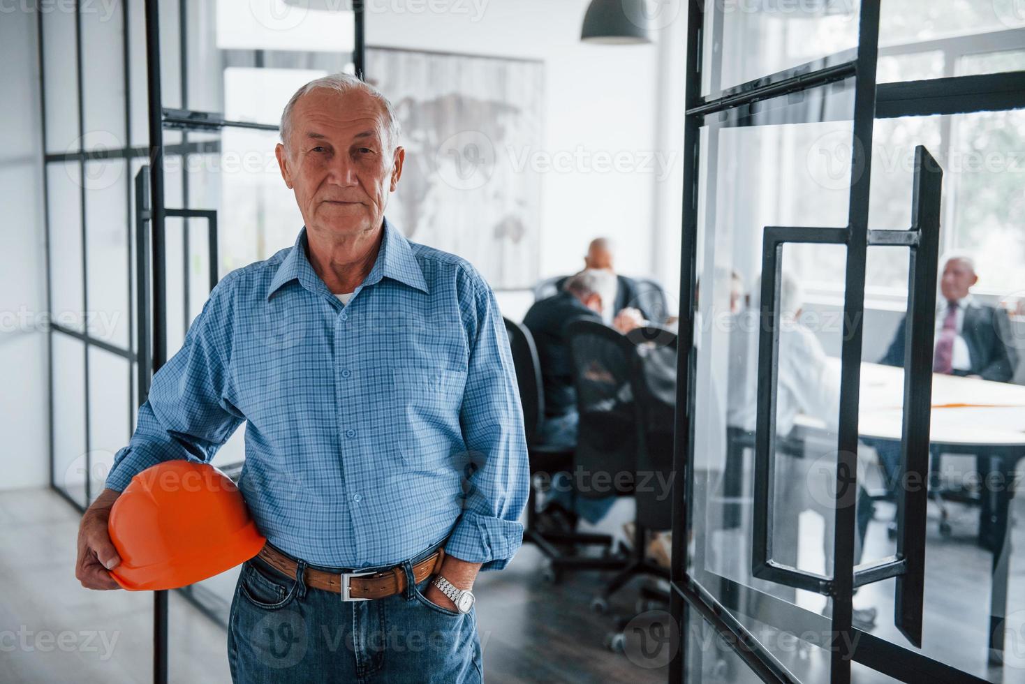Portrait of senior man that stands in front of aged team of elderly businessman architects that have a meeting in the office photo