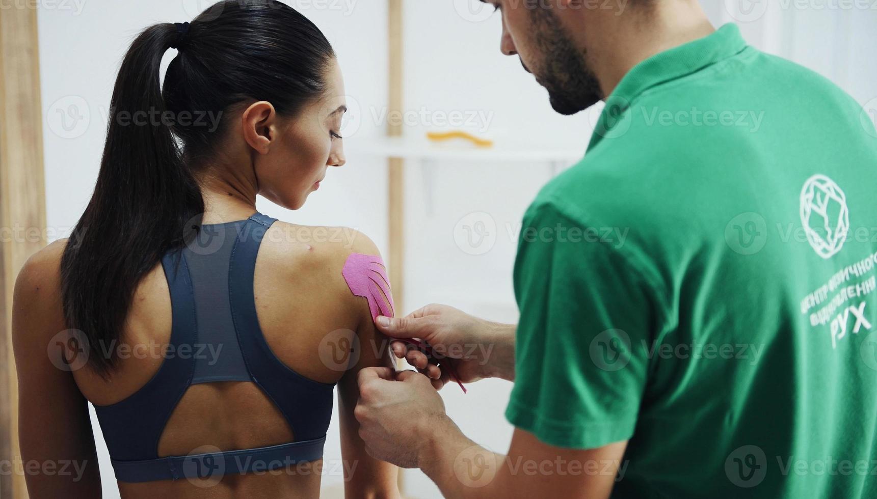 Doctor helps woman by shoulder treatment with kinesio tape photo