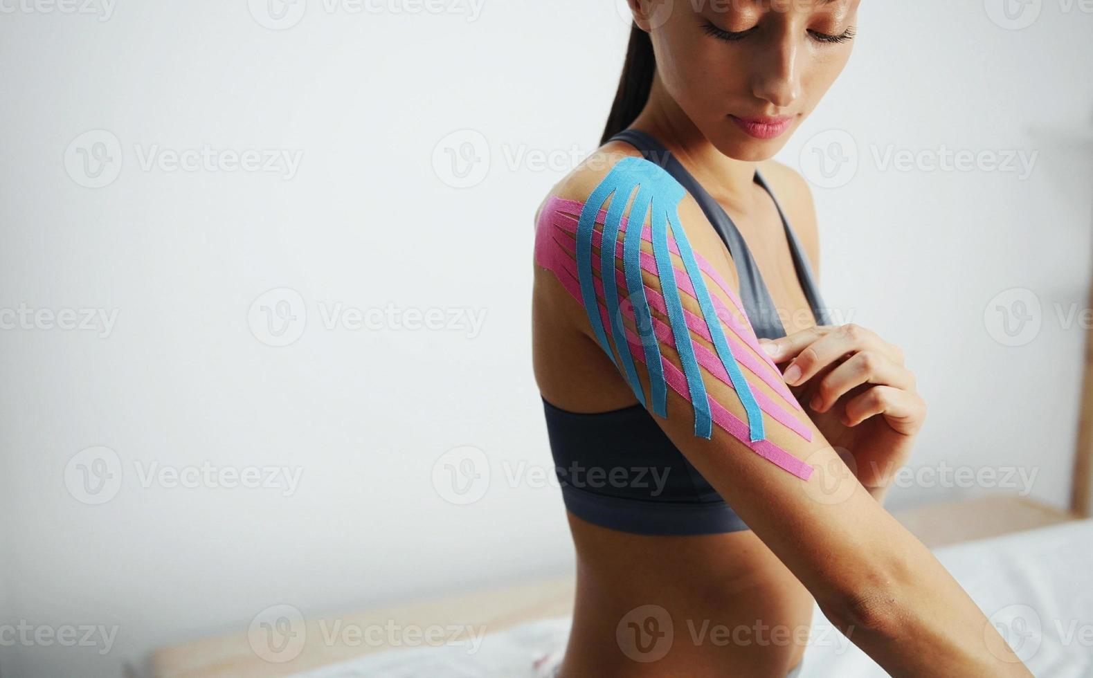 Sportive woman sits indoors with kinesio tape on her shoulder photo