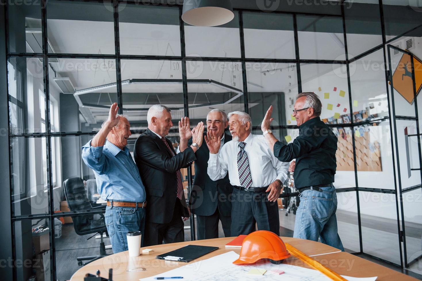 Job well done, gives high five to each other. Aged team of elderly businessman architects stands in the office together photo