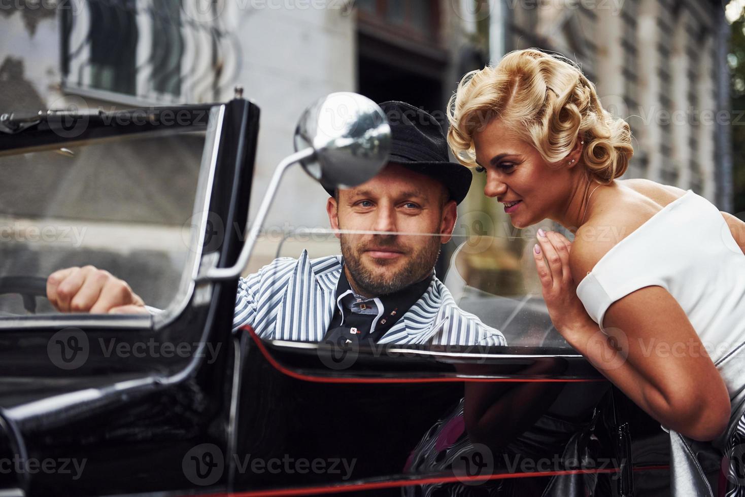 Beautiful couple in old fashioned wear is in city with retro car photo
