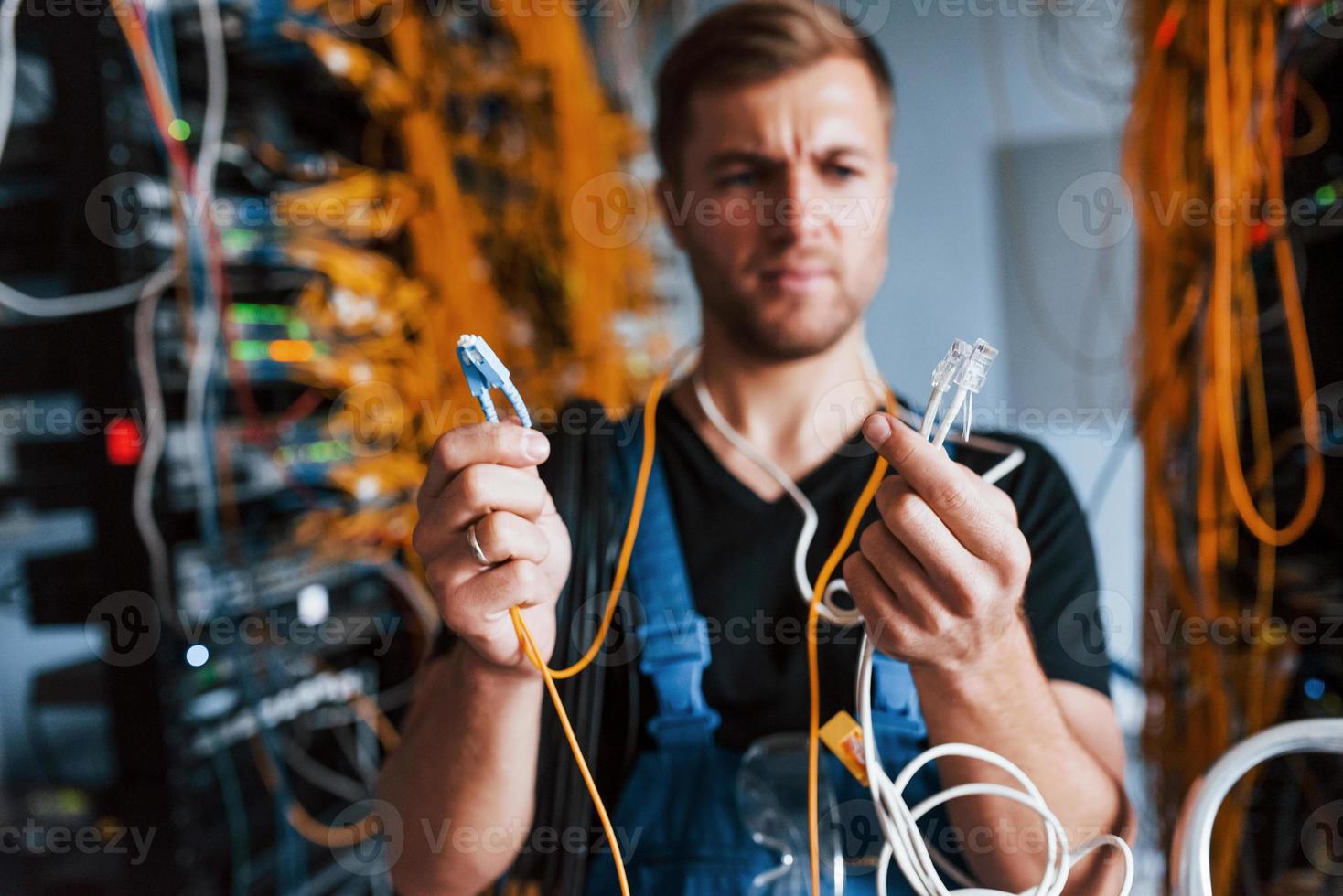 Young man in uniform feels confused and looking for a solution with internet equipment and wires in server room photo