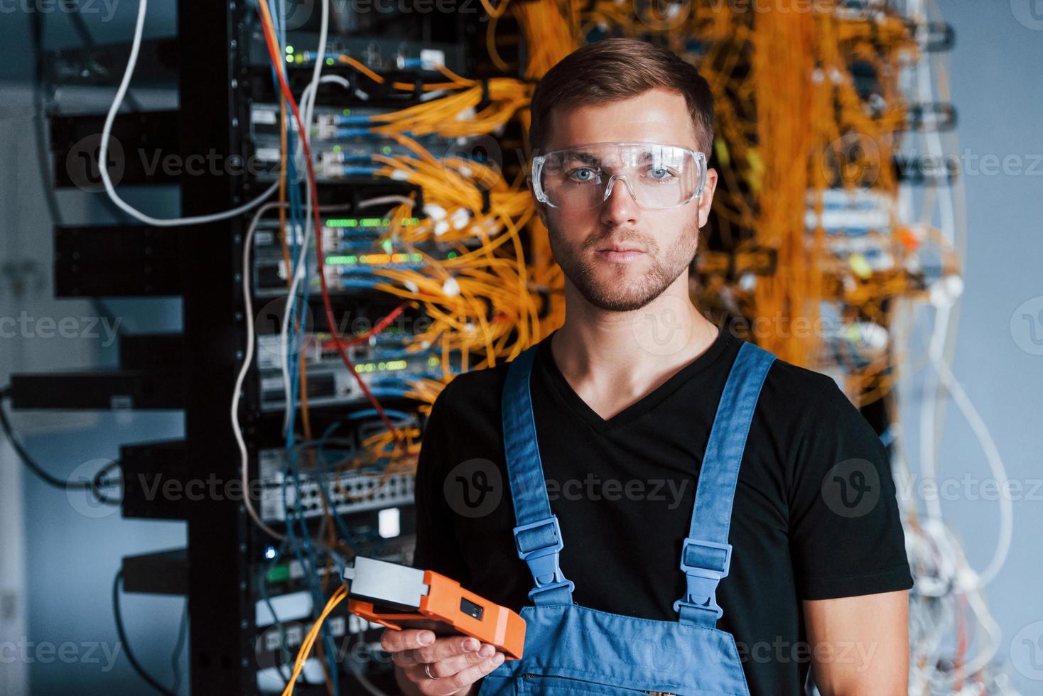 Young man in protective glasses works with internet equipment and wires in server room photo