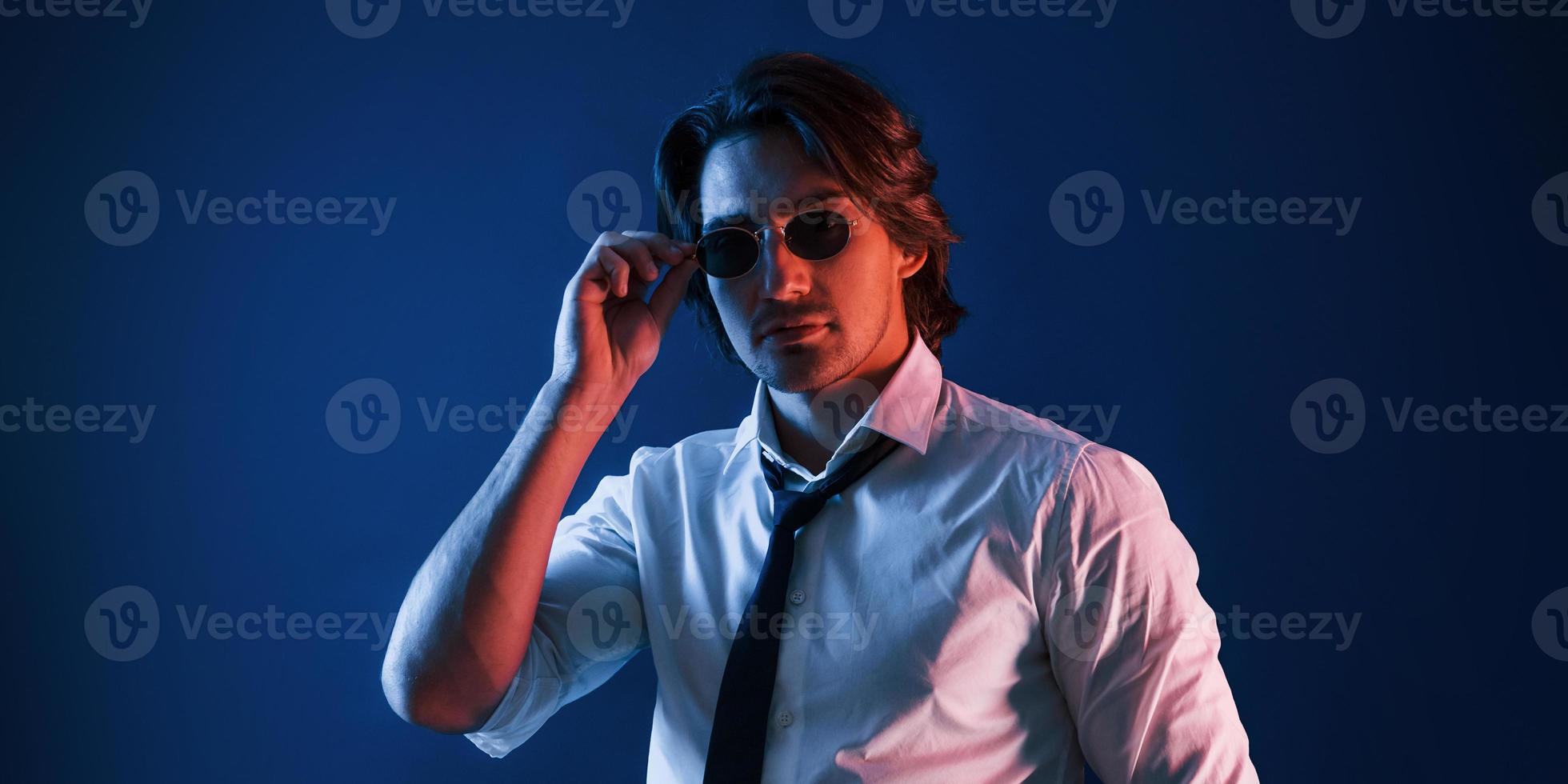 Beautiful man in formal wear and in glasses is in the studio with blue neon lighting photo