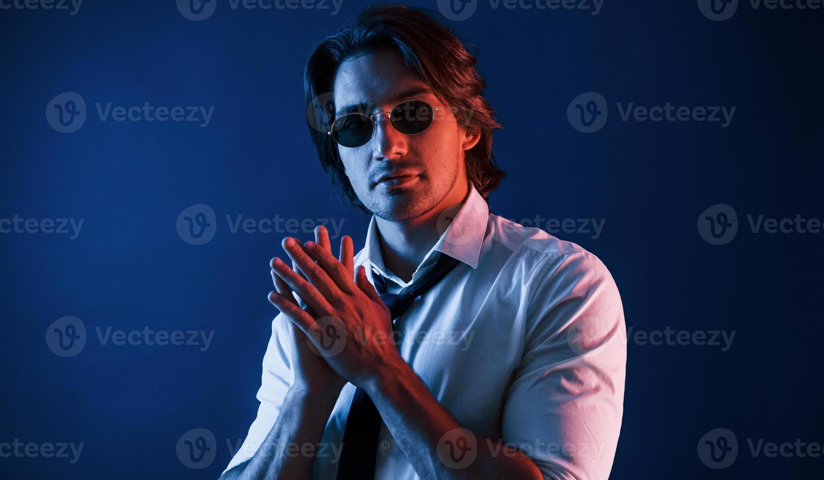 Beautiful man in formal wear and in glasses is in the studio with blue neon lighting photo