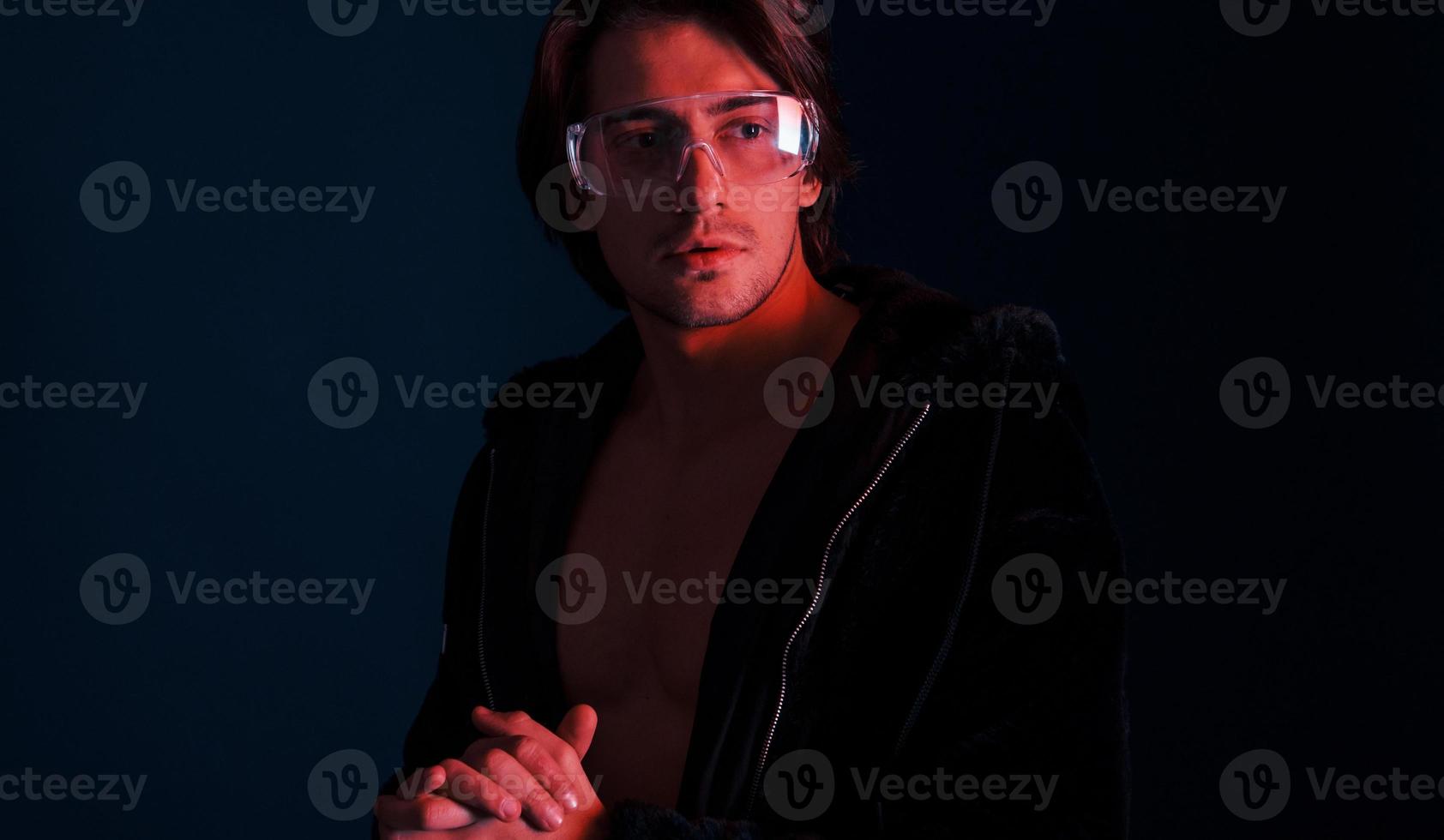 Beautiful long haired hot man in glasses is in the studio with blue neon lighting photo