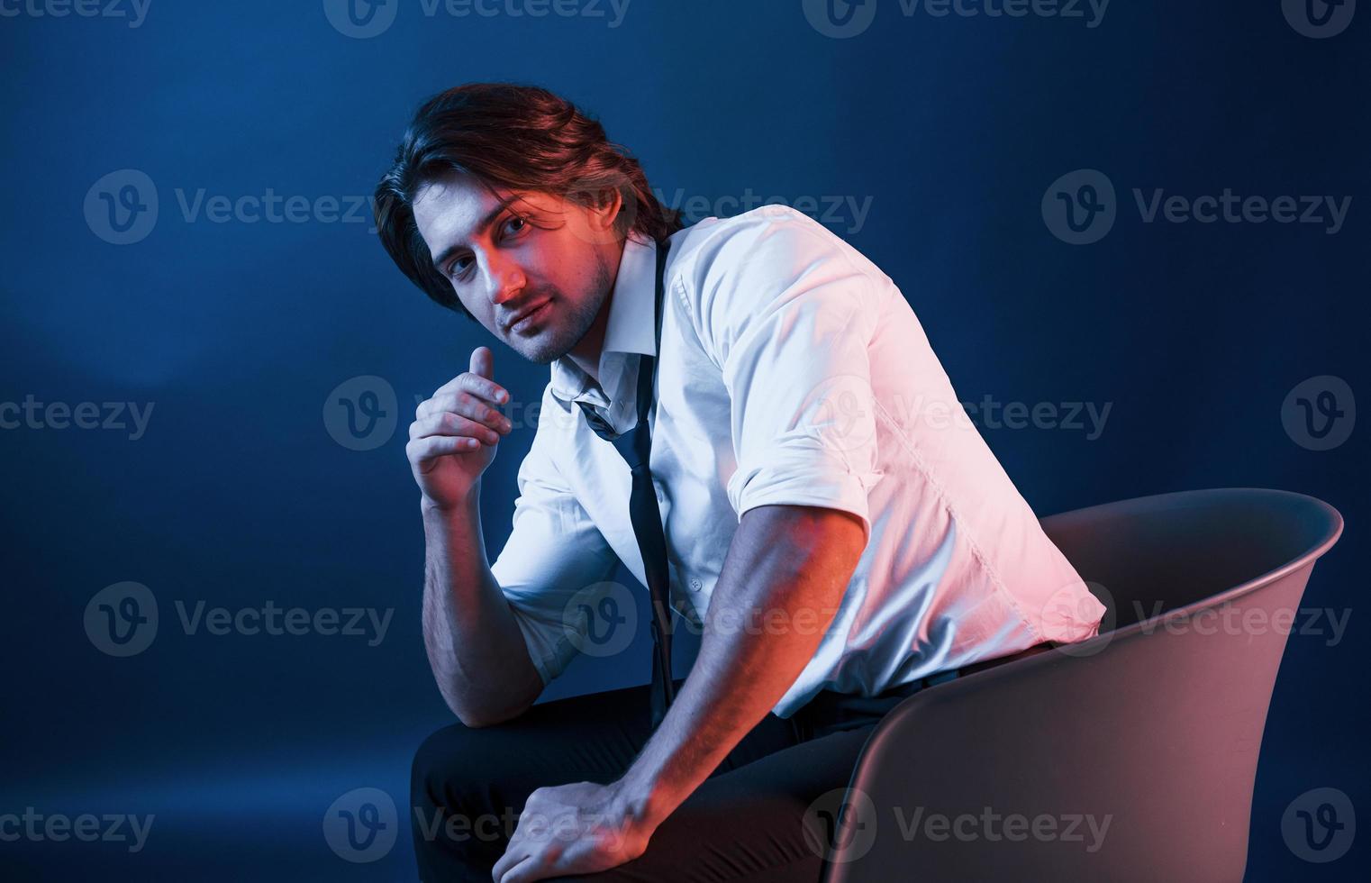 Beautiful man in glasses sits in the studio with blue neon lighting photo