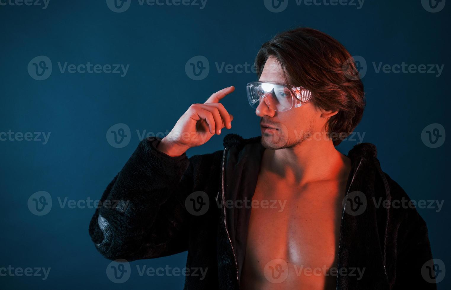 Beautiful long haired hot man in glasses is in the studio with blue neon lighting photo