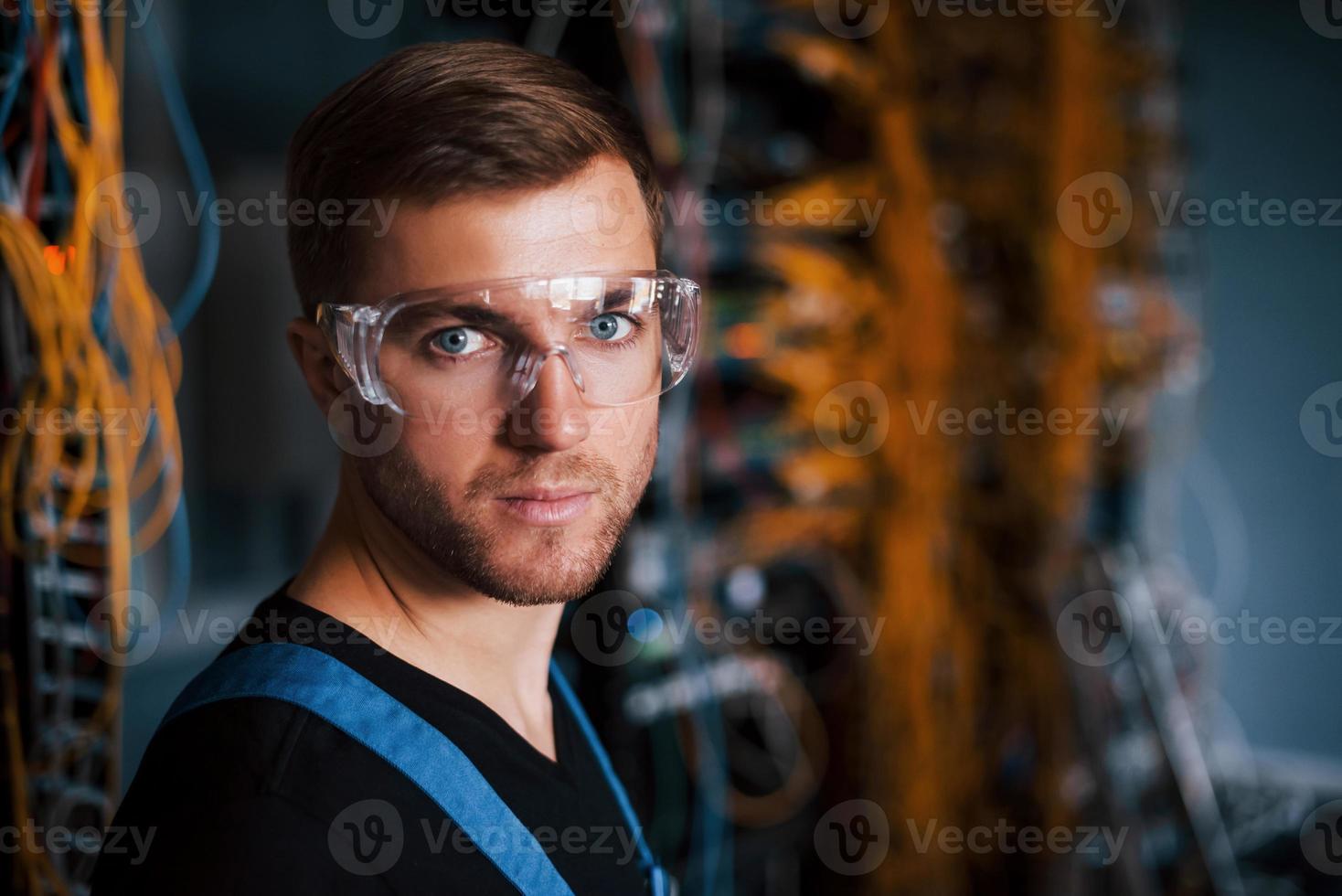 Young man in uniform works with internet equipment and wires in server room photo