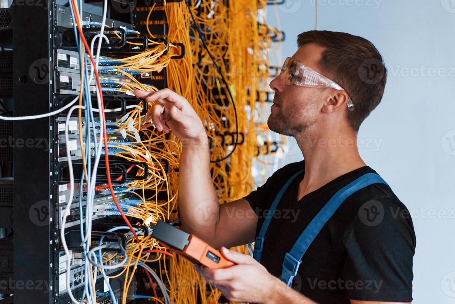 Young man in protective glasses works with internet equipment and wires in server room photo