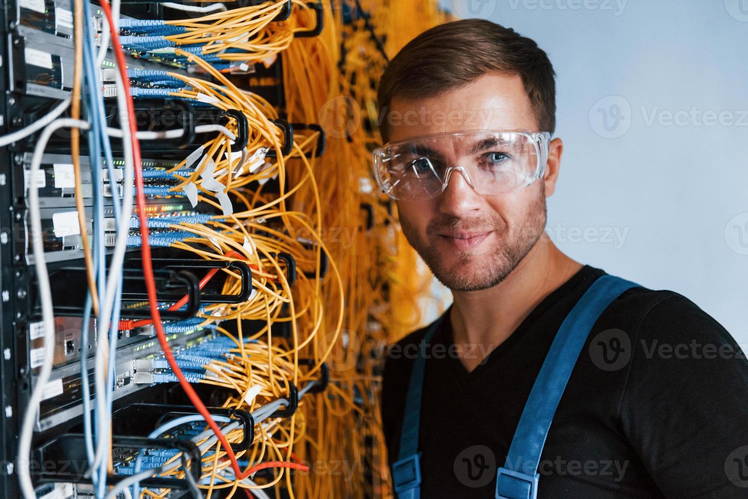 Young man in protective glasses works with internet equipment and wires in server room photo