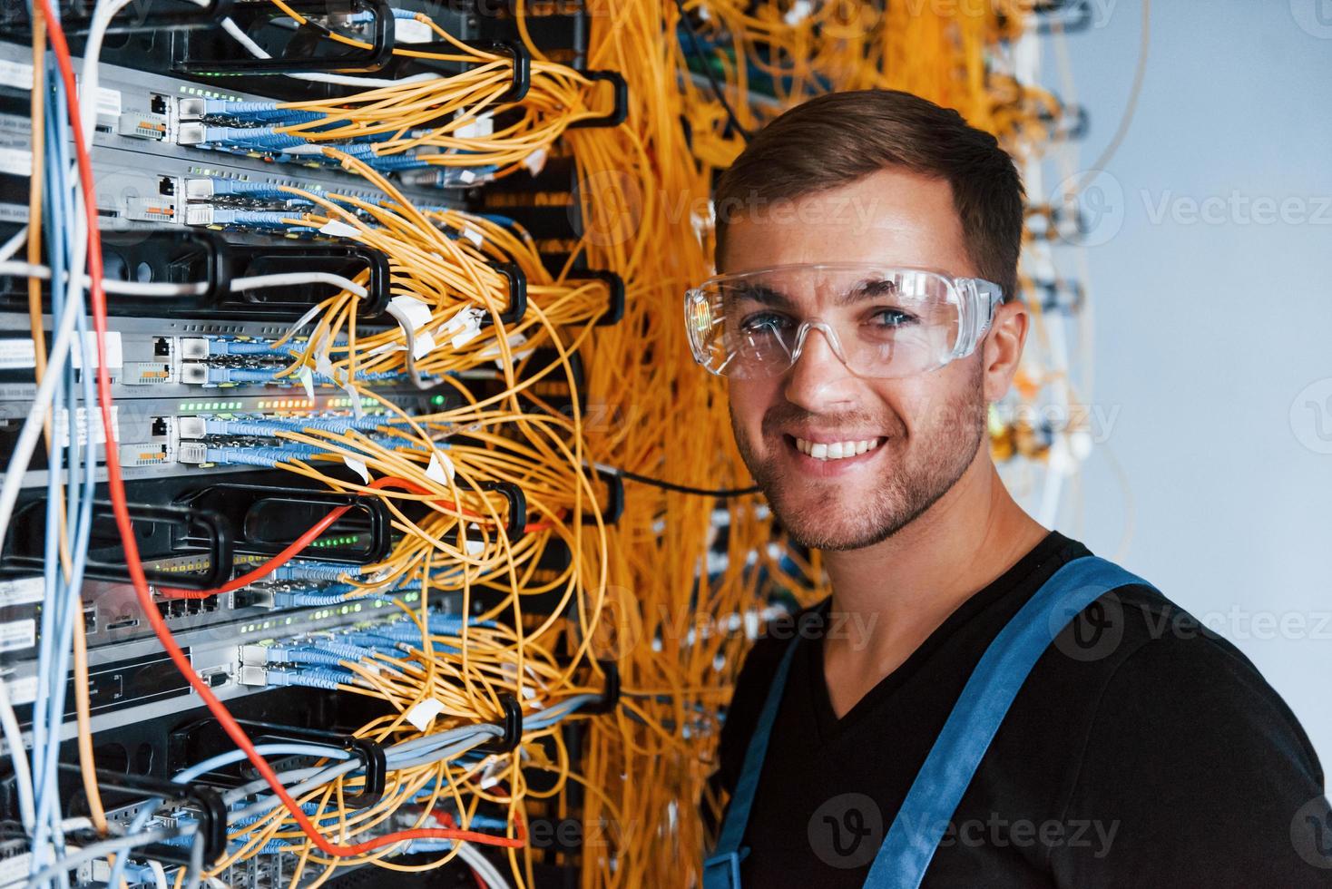 Young man in protective glasses works with internet equipment and wires in server room photo