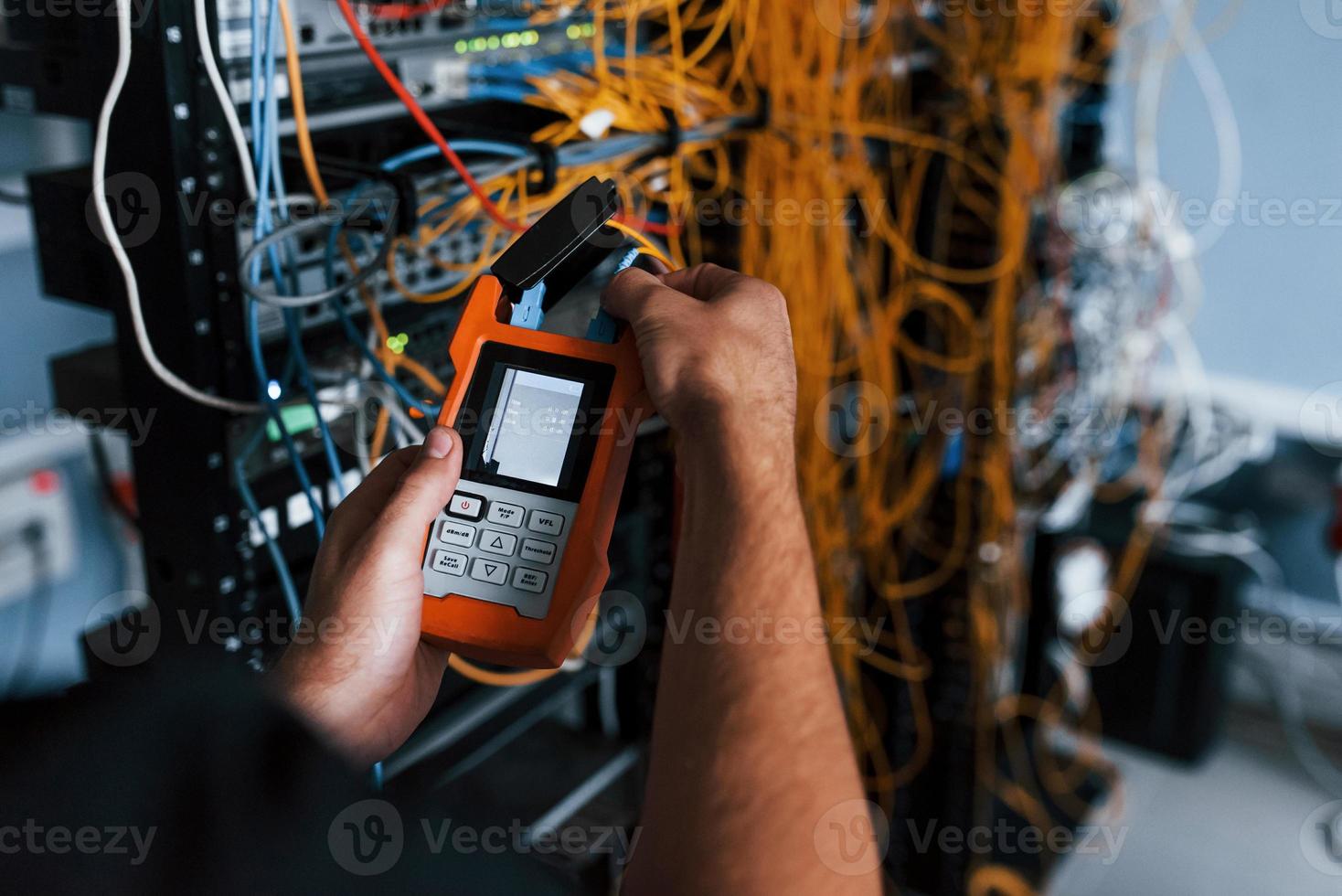 Young man withj measuring device in hands works with internet equipment and wires in server room photo