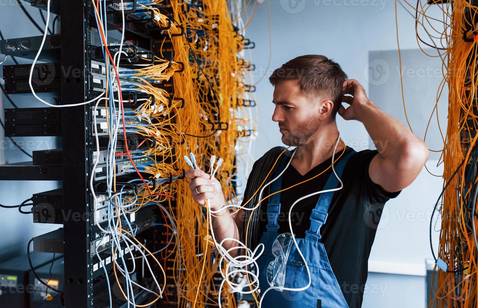Young man in uniform feels confused and looking for a solution with internet equipment and wires in server room photo