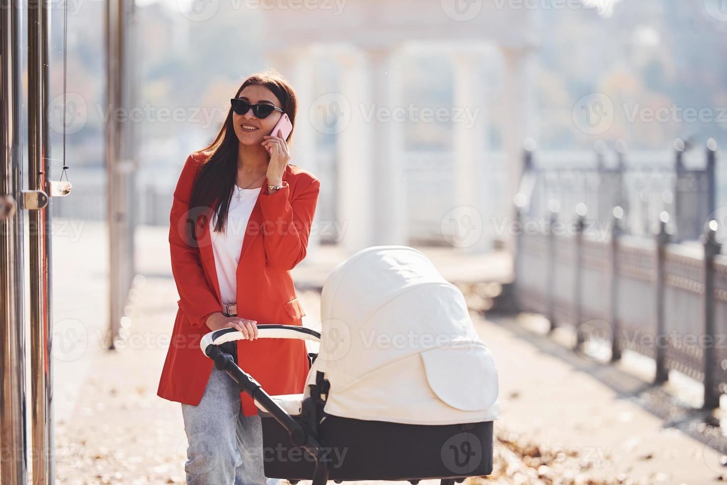 Mother in red coat have a walk with her kid in the pram in the park at autumn time photo