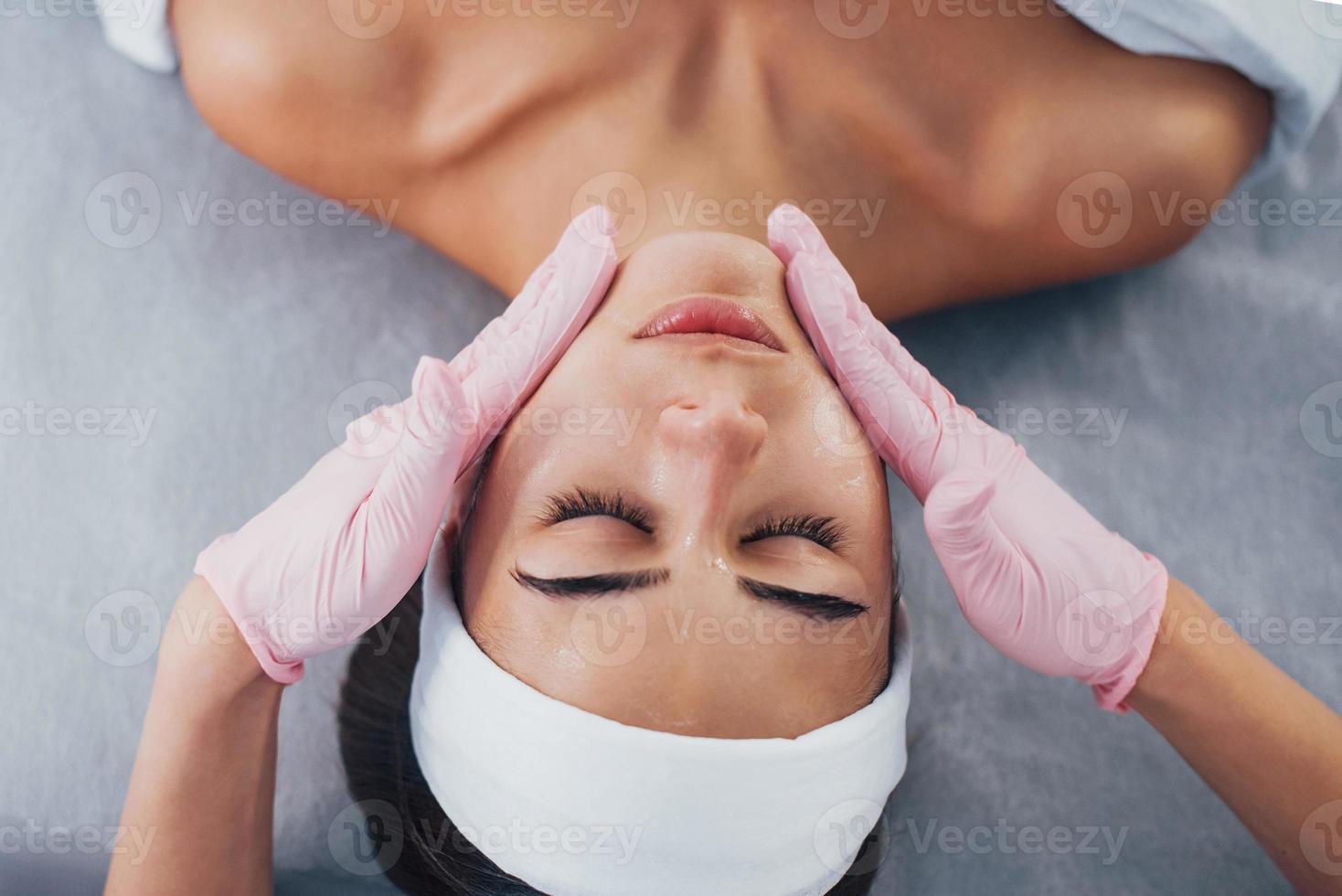 vista de cerca de la mujer que se acuesta en el salón de spa y tiene un procedimiento de limpieza facial foto