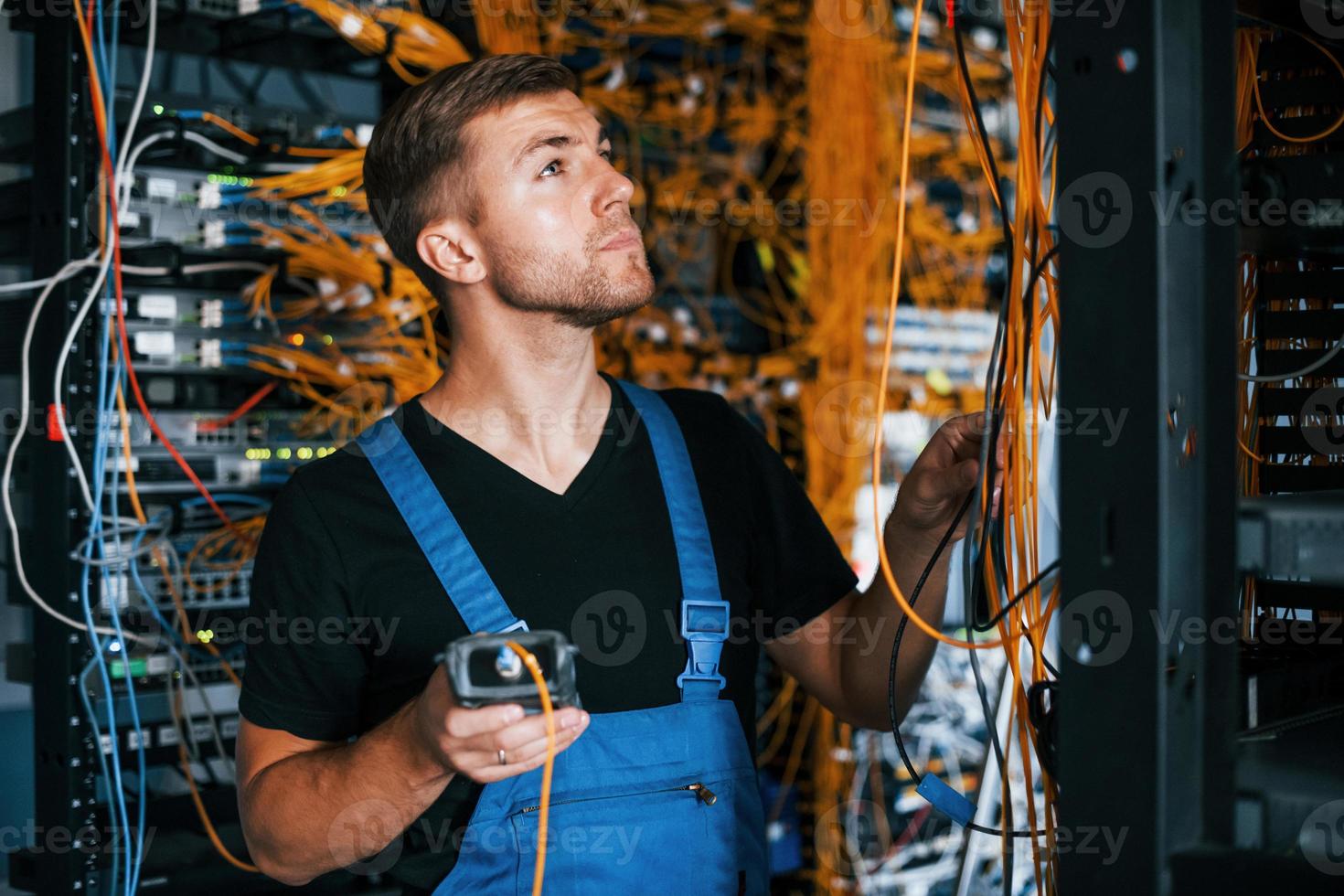 un joven uniformado tiene un trabajo con equipos de internet y cables en la sala de servidores foto