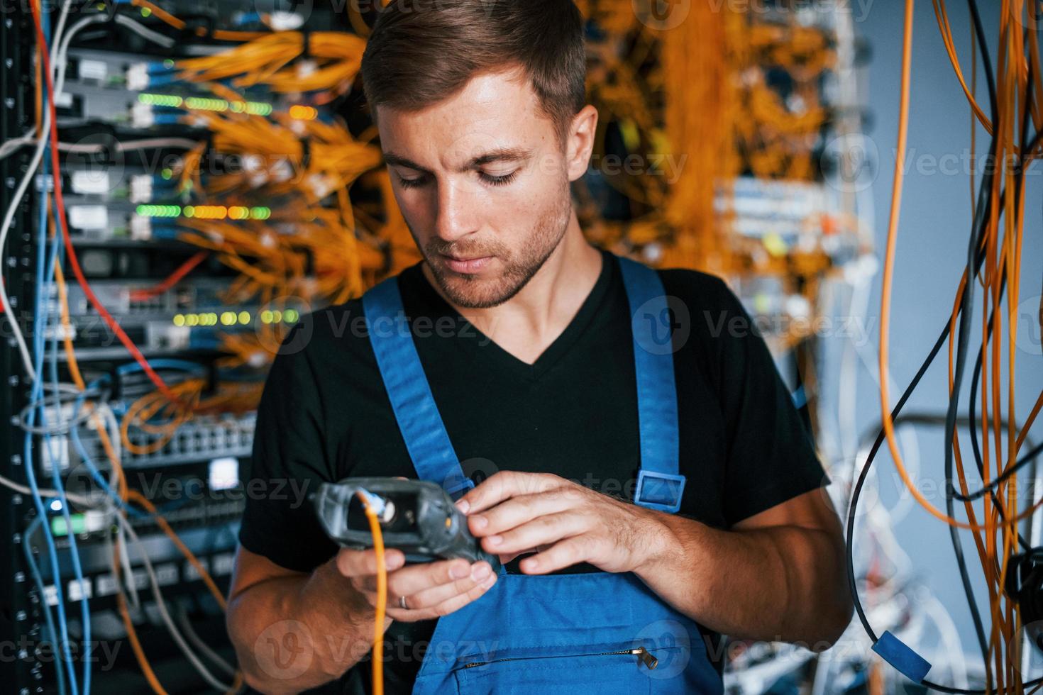 un joven uniformado tiene un trabajo con equipos de internet y cables en la sala de servidores foto