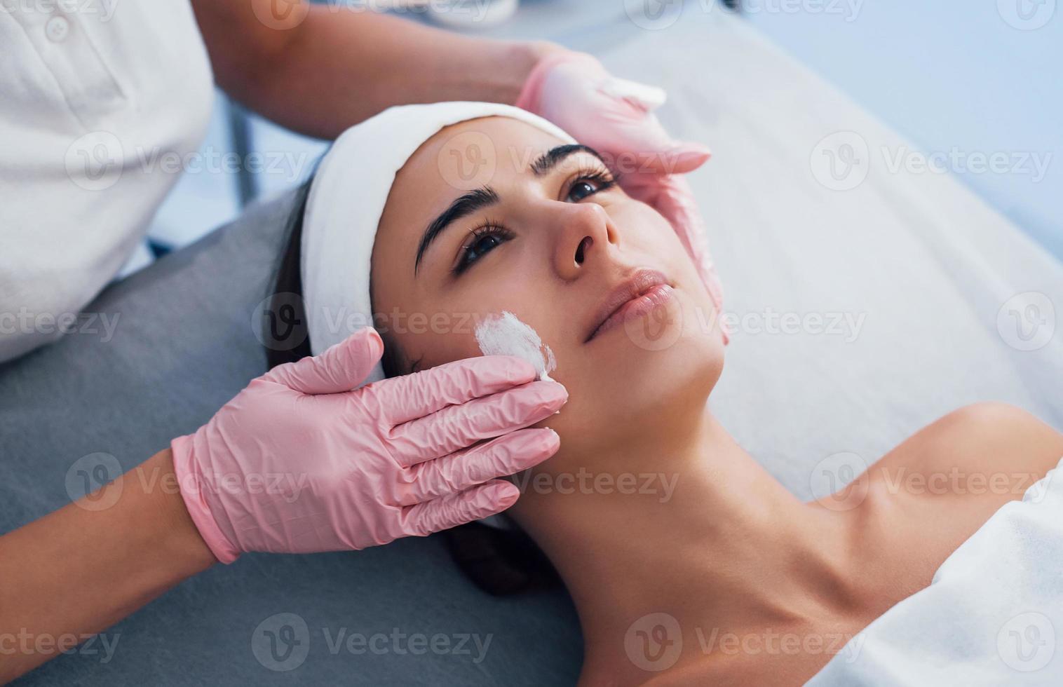 vista de cerca de la mujer que se acuesta en el salón de spa y tiene un procedimiento de limpieza facial con la máscara foto