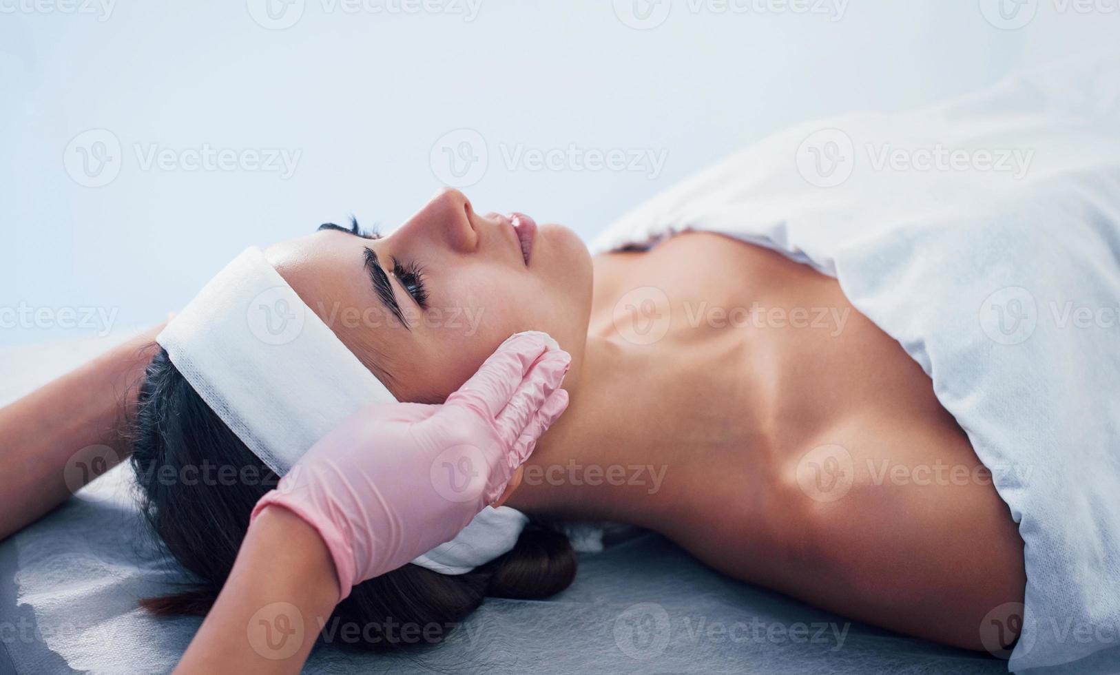 Close up view of woman that lying down in spa salon and have face cleaning procedure by cosmetologist in gloves photo