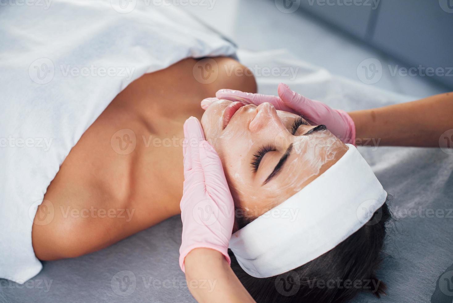 vista de cerca de la mujer que se acuesta en el salón de spa y tiene un procedimiento de limpieza facial con la máscara foto