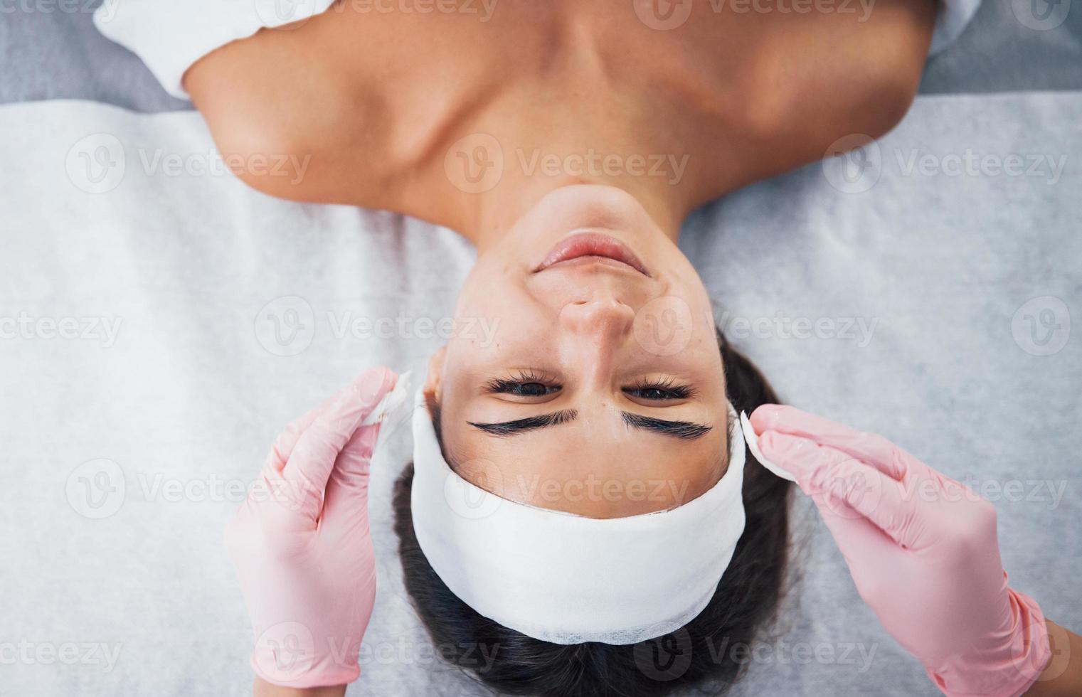 Close up view of woman that lying down in spa salon and have face cleaning procedure by cosmetologist in gloves photo