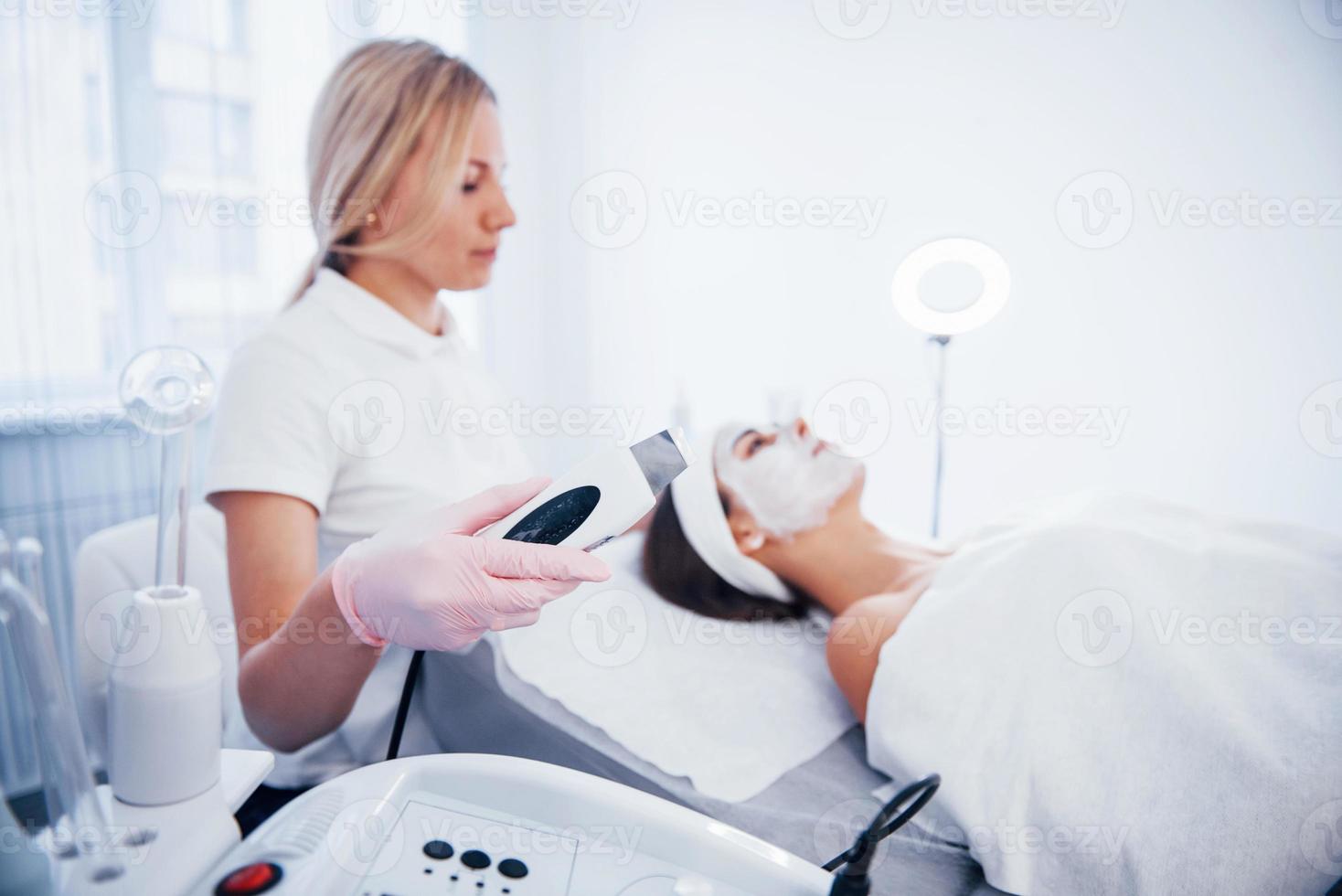 Woman lying down in spa salon and have face cleaning procedure by professional cosmetologist photo