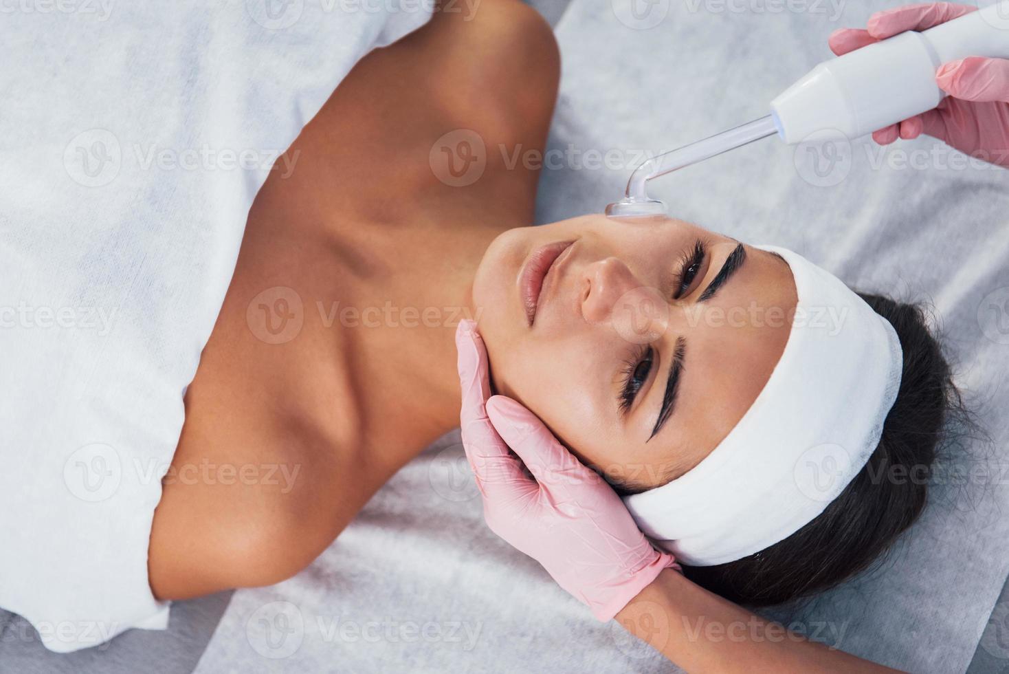 vista de cerca de la mujer que se acuesta en el salón de spa y tiene un procedimiento de limpieza facial usando un dispositivo moderno foto