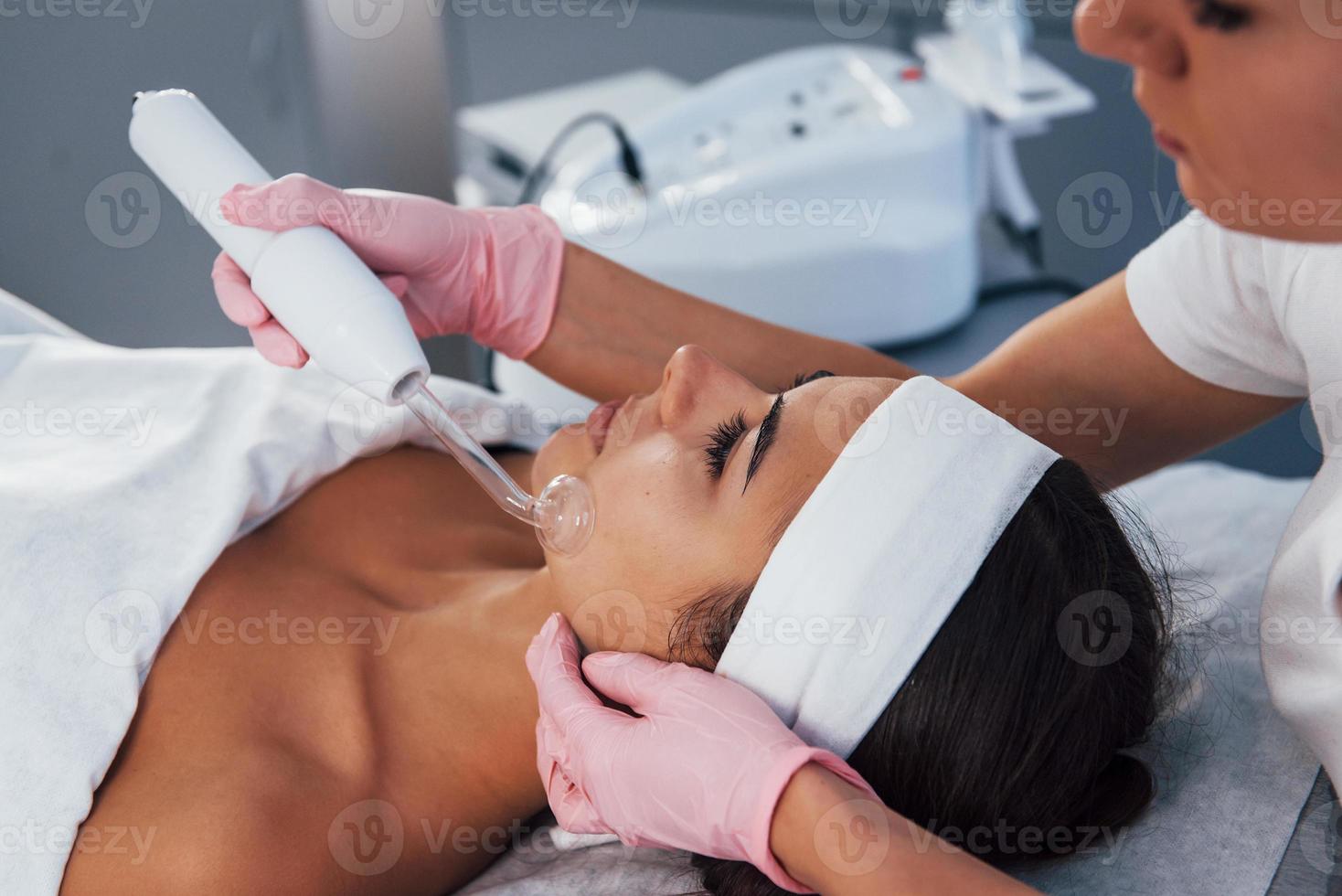 vista de cerca de la mujer que se acuesta en el salón de spa y tiene un procedimiento de limpieza facial usando un dispositivo moderno foto