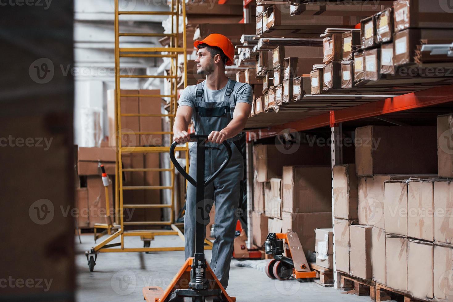 Young male worker in uniform is in the warehouse with pallet truck photo