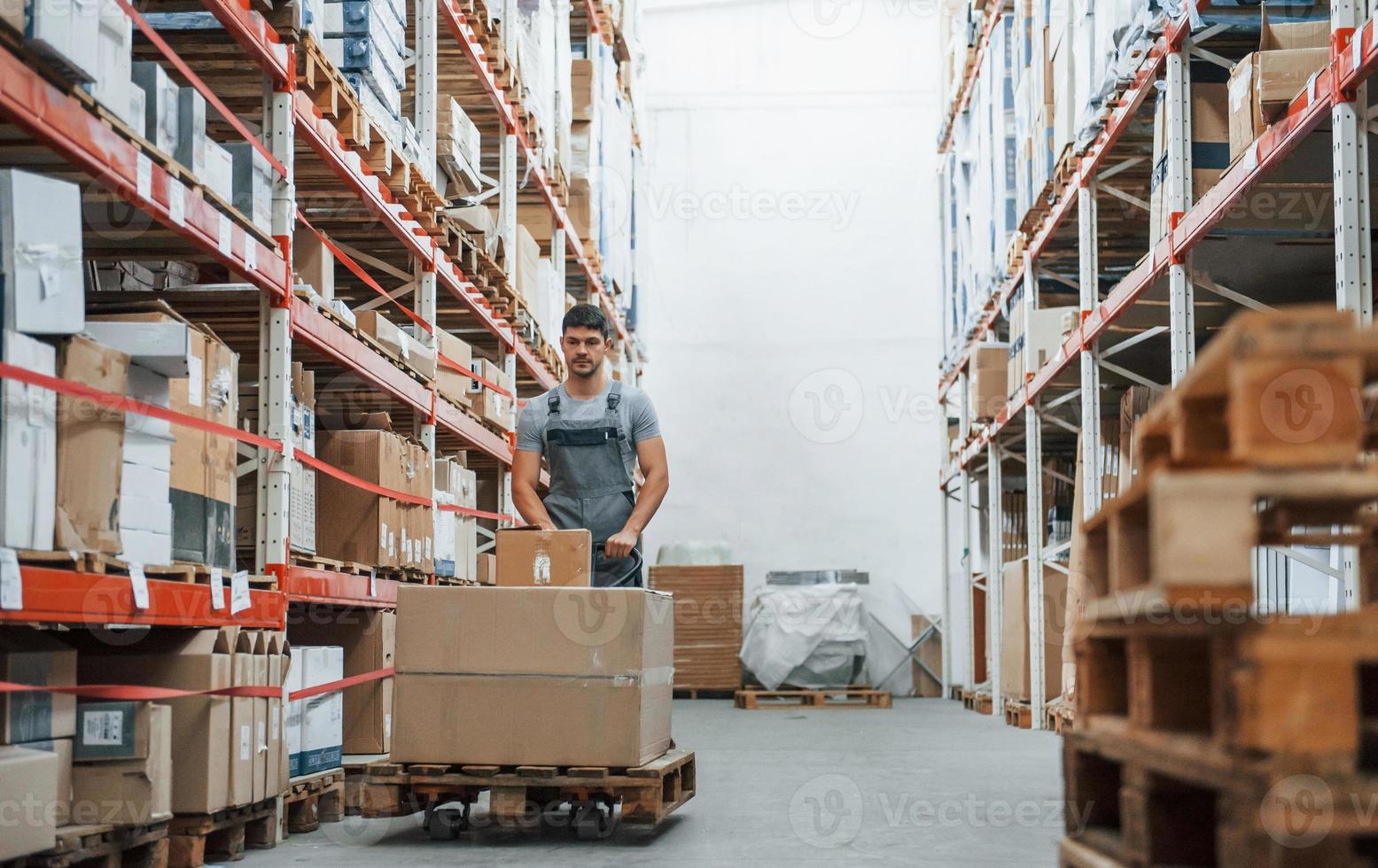 Young male worker in uniform is in the warehouse pushing pallet truck photo